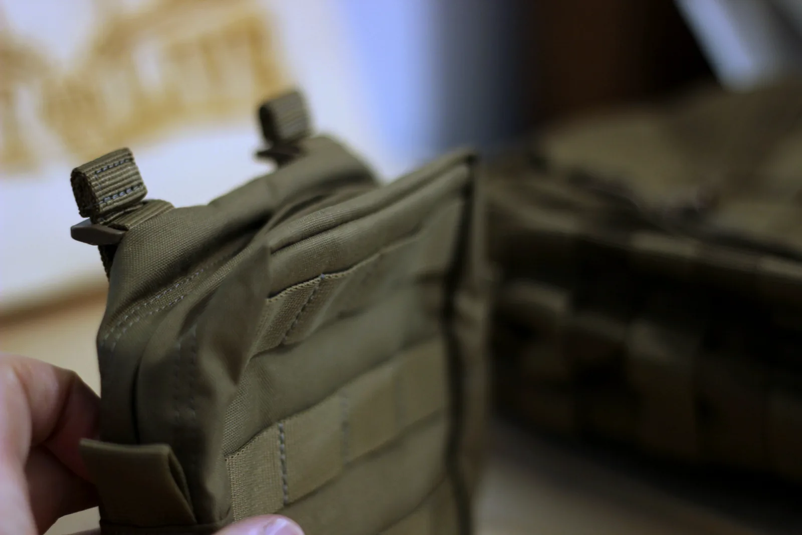 The 6.6 pouch held in one hand showing its MOLLE face and mounting straps