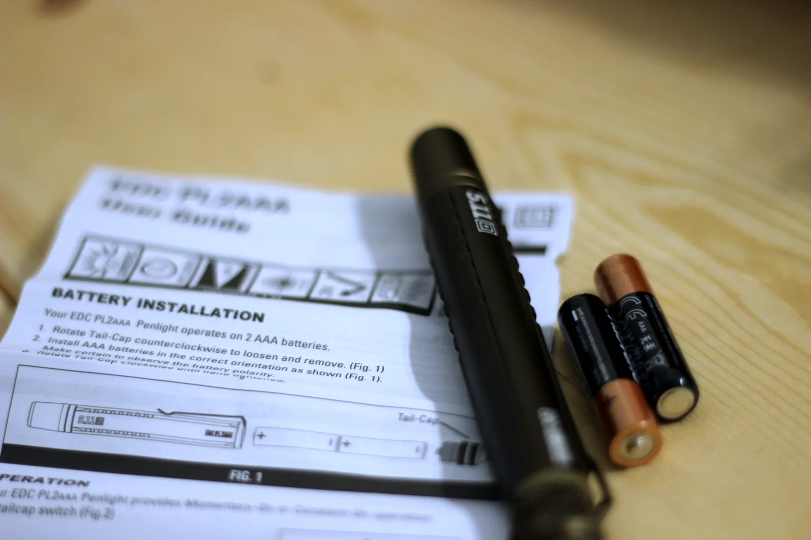 The flashlight body beside its folded user guide and two AAA batteries on a bench