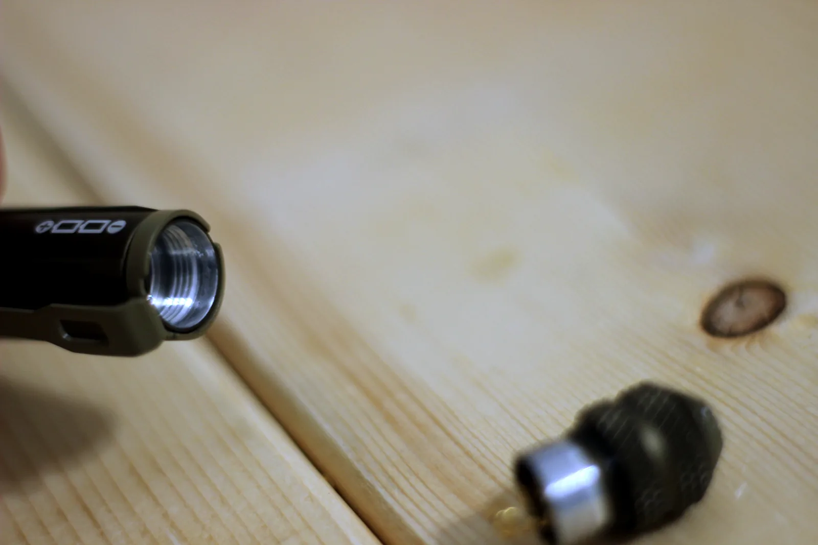 The head of the flashlight and its tail cap separated on a wooden bench
