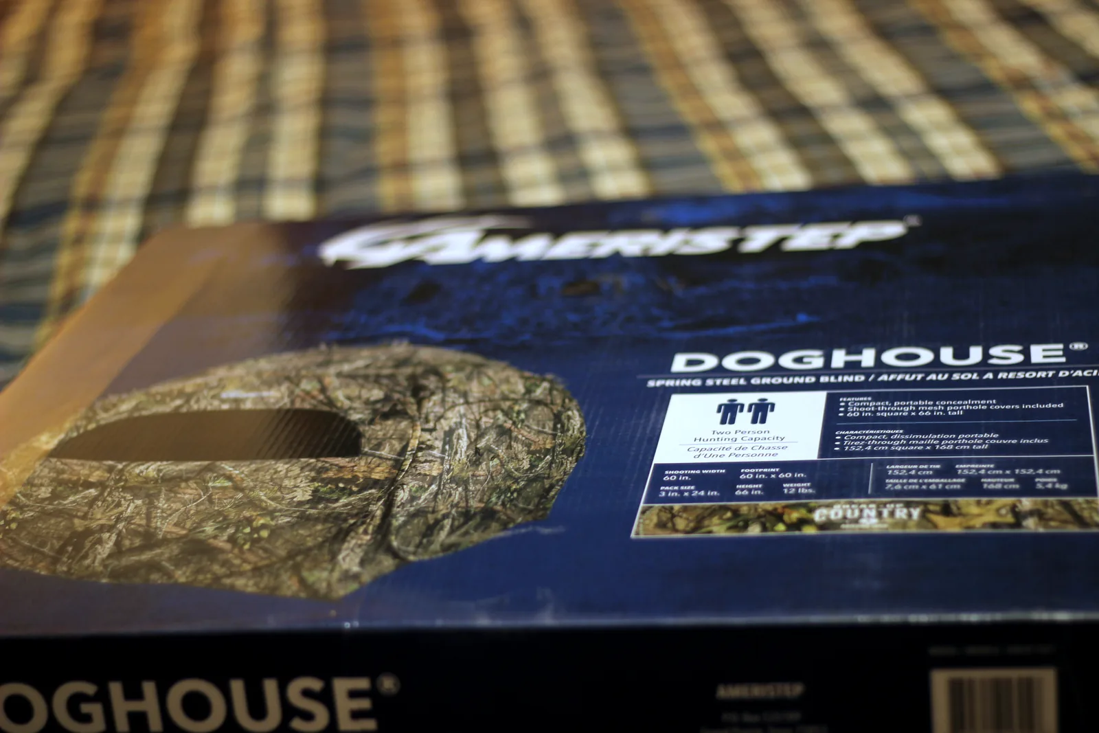 The Ameristep Doghouse carton on a plaid blanket, printed with the blind and the Ameristep logo