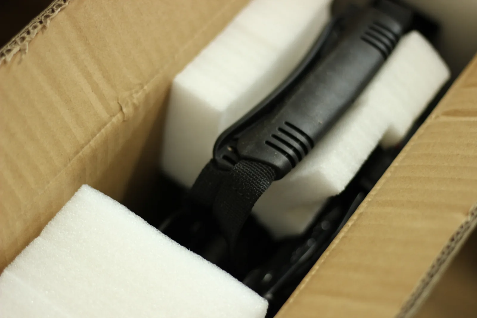 The carton opened showing white foam blocks packed around the folded panel and its black carry handle