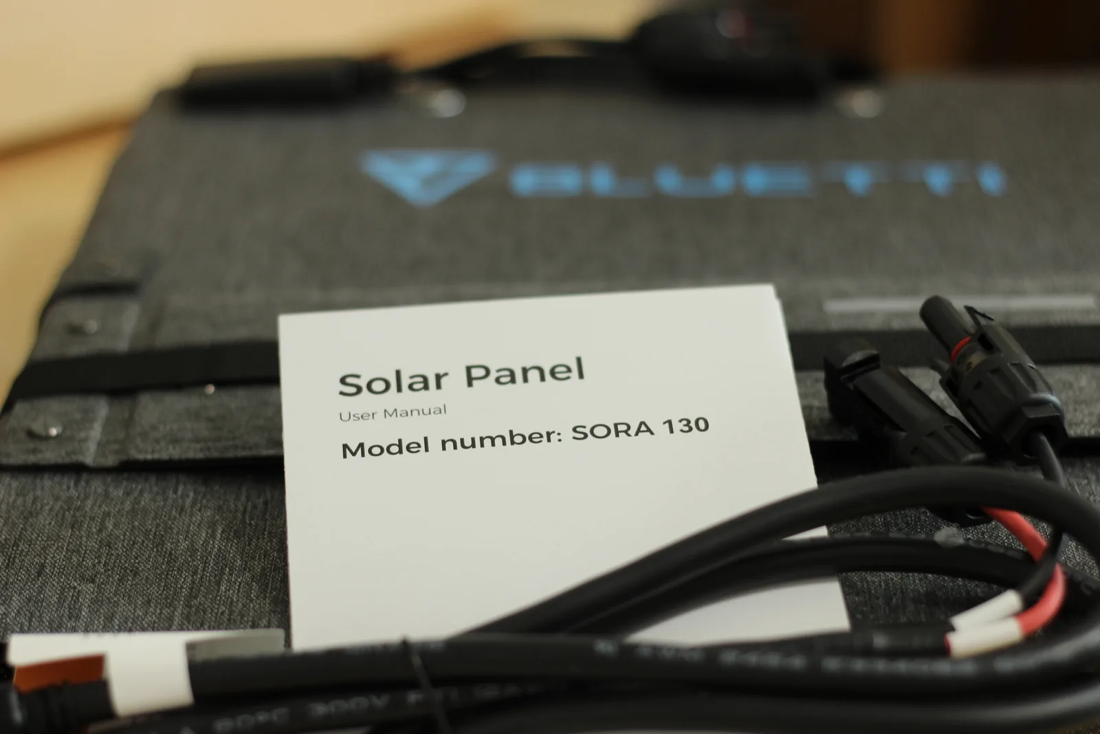 The user manual lying on the folded grey panel, reading Solar Panel, User Manual, Model number: SORA 130, with the MC4 leads coiled alongside