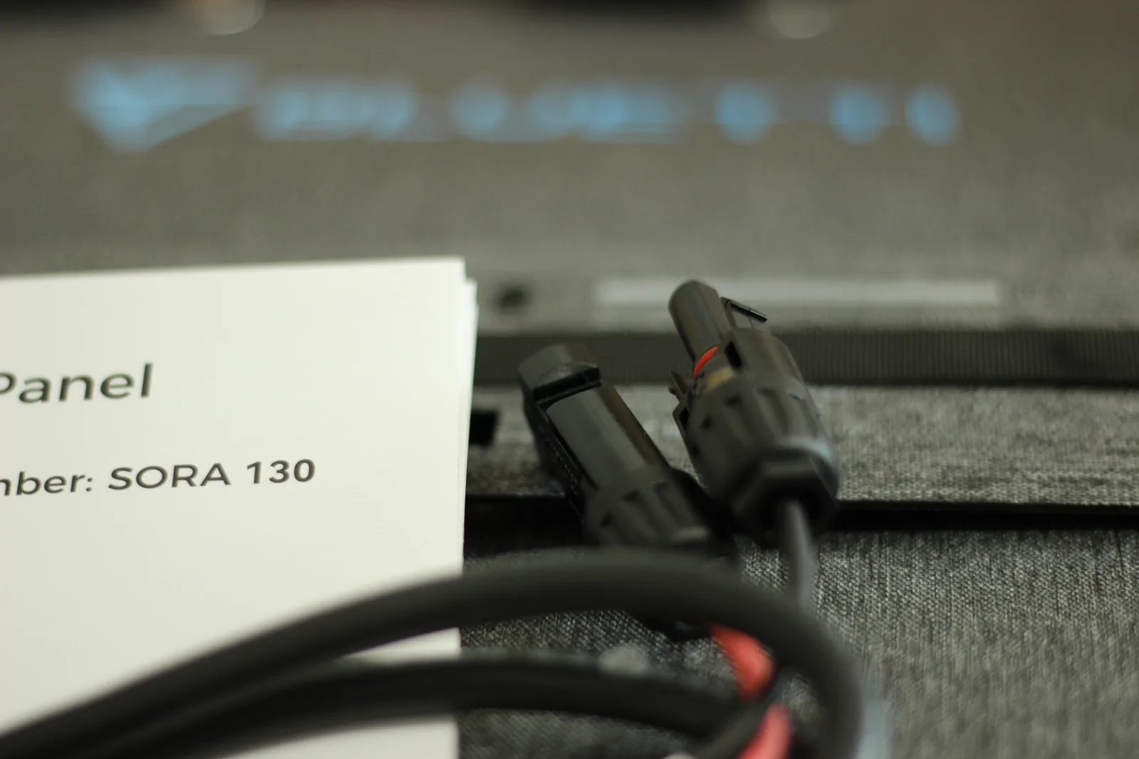 The two MC4 connectors on their black cables resting on the panel's grey fabric case beside the manual