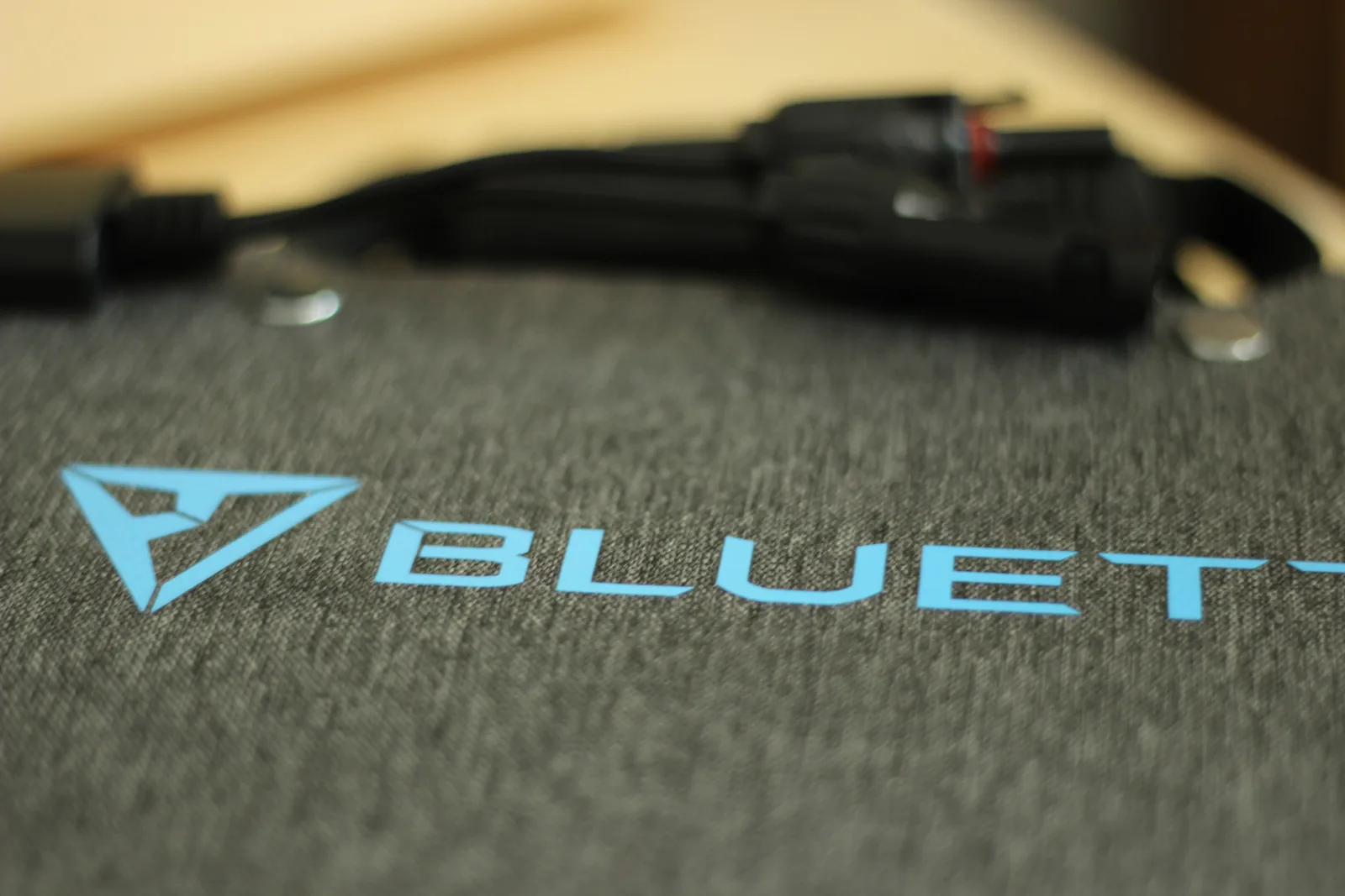 The blue BLUETTI logo printed on the grey heathered fabric back of the folded panel with cables above