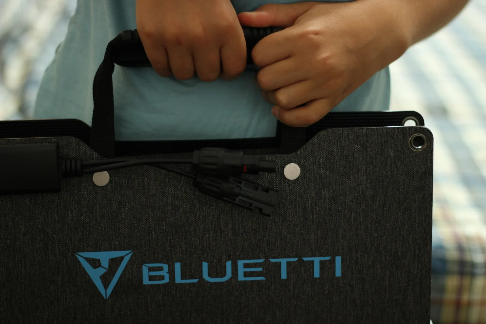 The folded panel carried at waist height by its webbing handle, MC4 leads clipped to the back