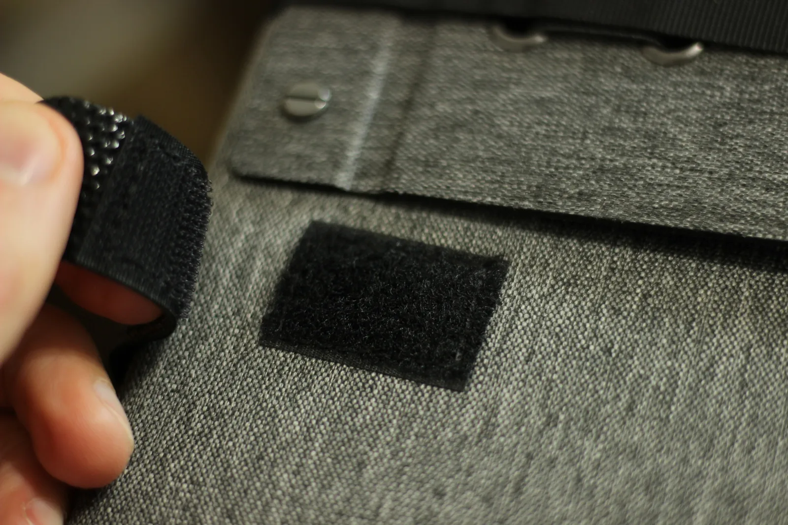 A hand lifting the hook-and-loop strap away from its mating patch on the panel case