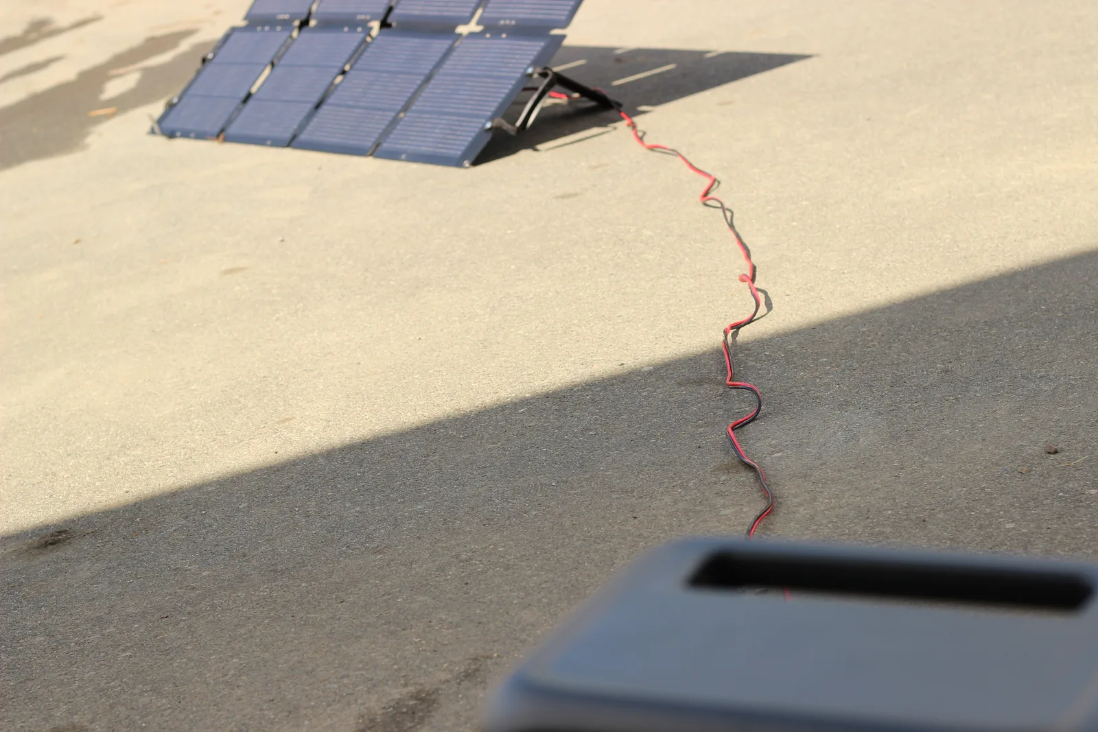 A red and black cable snaking across a sunlit concrete driveway from the panel in the distance to the power station
