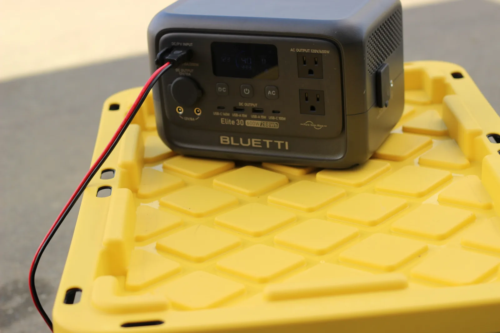 The BLUETTI Elite 30 on a yellow tote lid on a driveway with the solar lead running out of frame