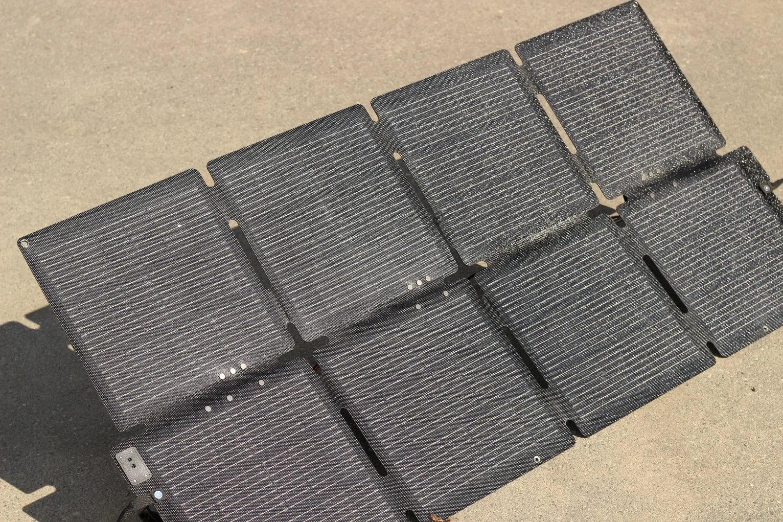 The solar panel laid completely flat on a concrete driveway showing all its cell sections