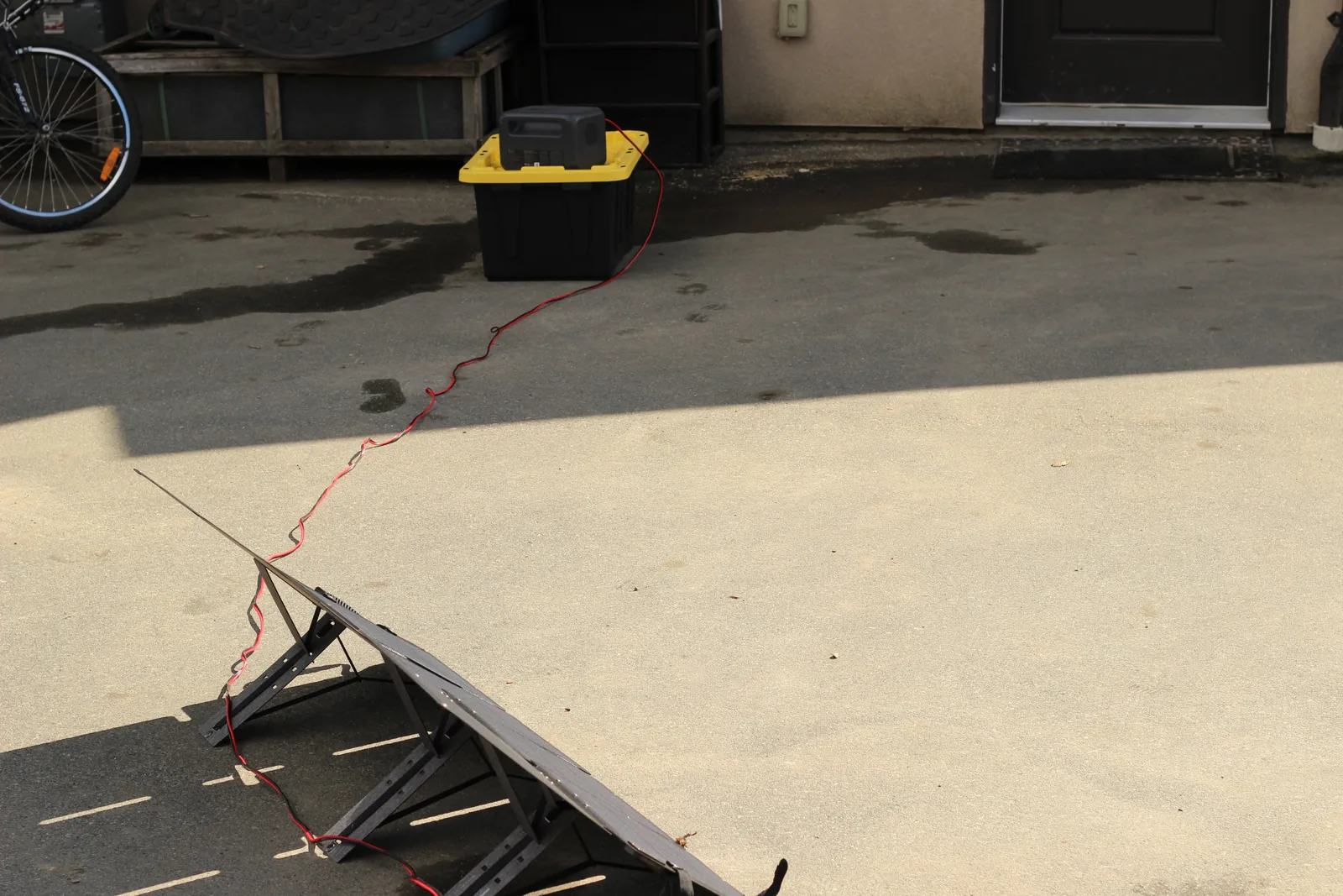 Wide view of the driveway with the panel at the bottom of frame and the power station on a tote by the house, cable running between