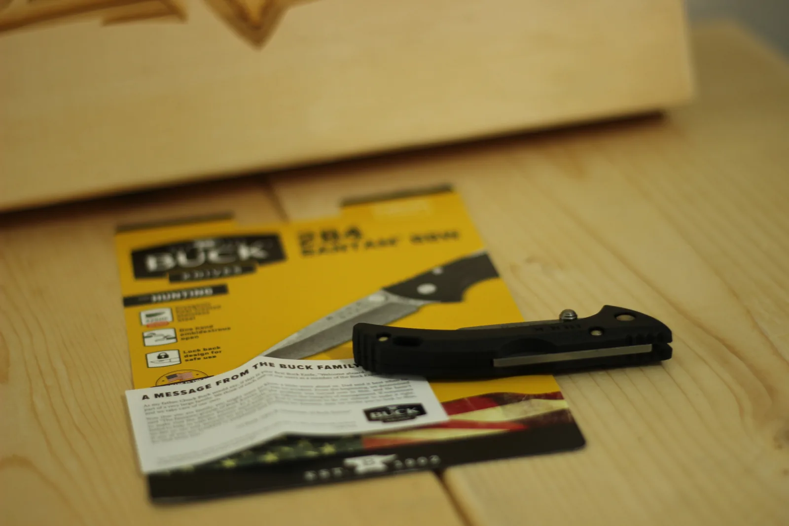 The closed knife and the printed cards laid out on a pale wooden bench with a laser-engraved wooden plaque behind