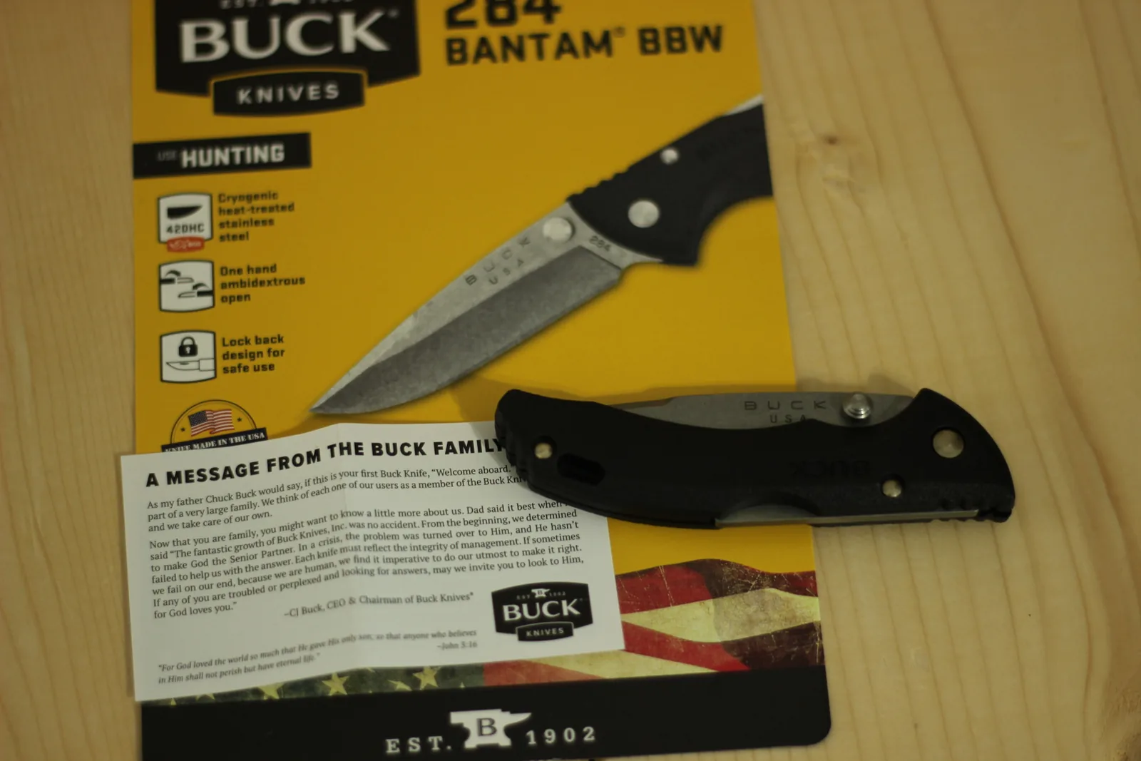 Overhead view of the yellow Buck card, the Buck family message slip, and the closed black knife on a wooden bench