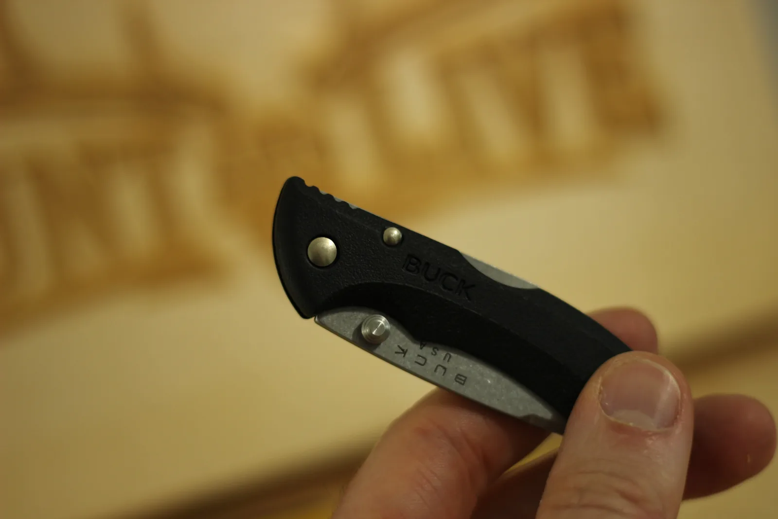The closed Bantam held between finger and thumb in front of a blurred laser-engraved wooden sign