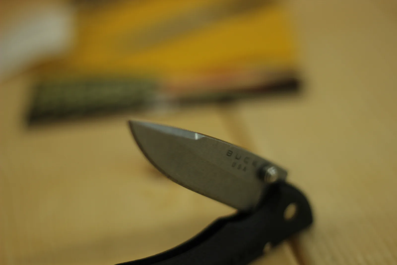 Close-up of the drop-point tip with the BUCK USA stamp partially in frame and the yellow packaging blurred behind