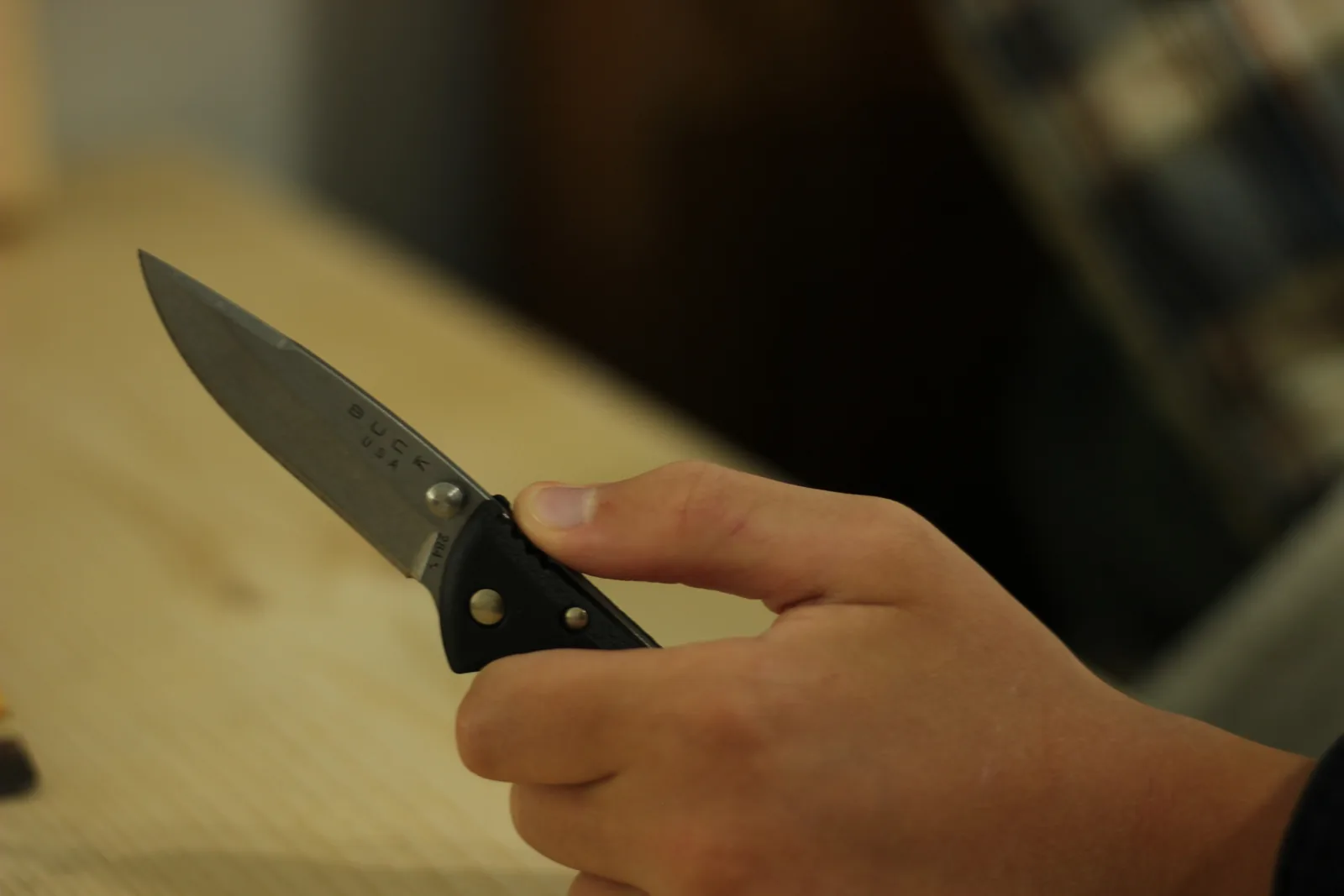 The open Bantam held in a hand above a pale wooden bench, blade pointing up and left