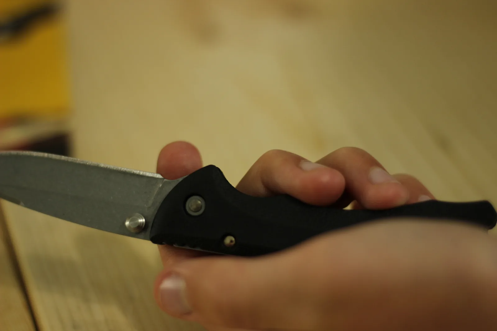A hand wrapped around the open knife in a forward grip with the blade extending left, fingers filling the whole handle