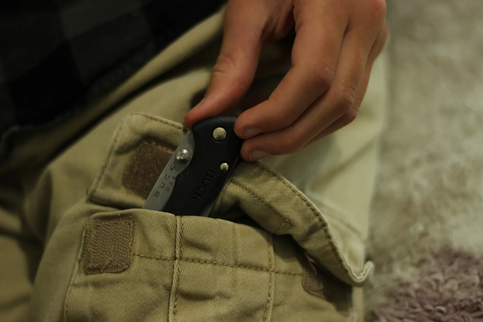 The closed knife being lowered into the pocket of a pair of tan trousers