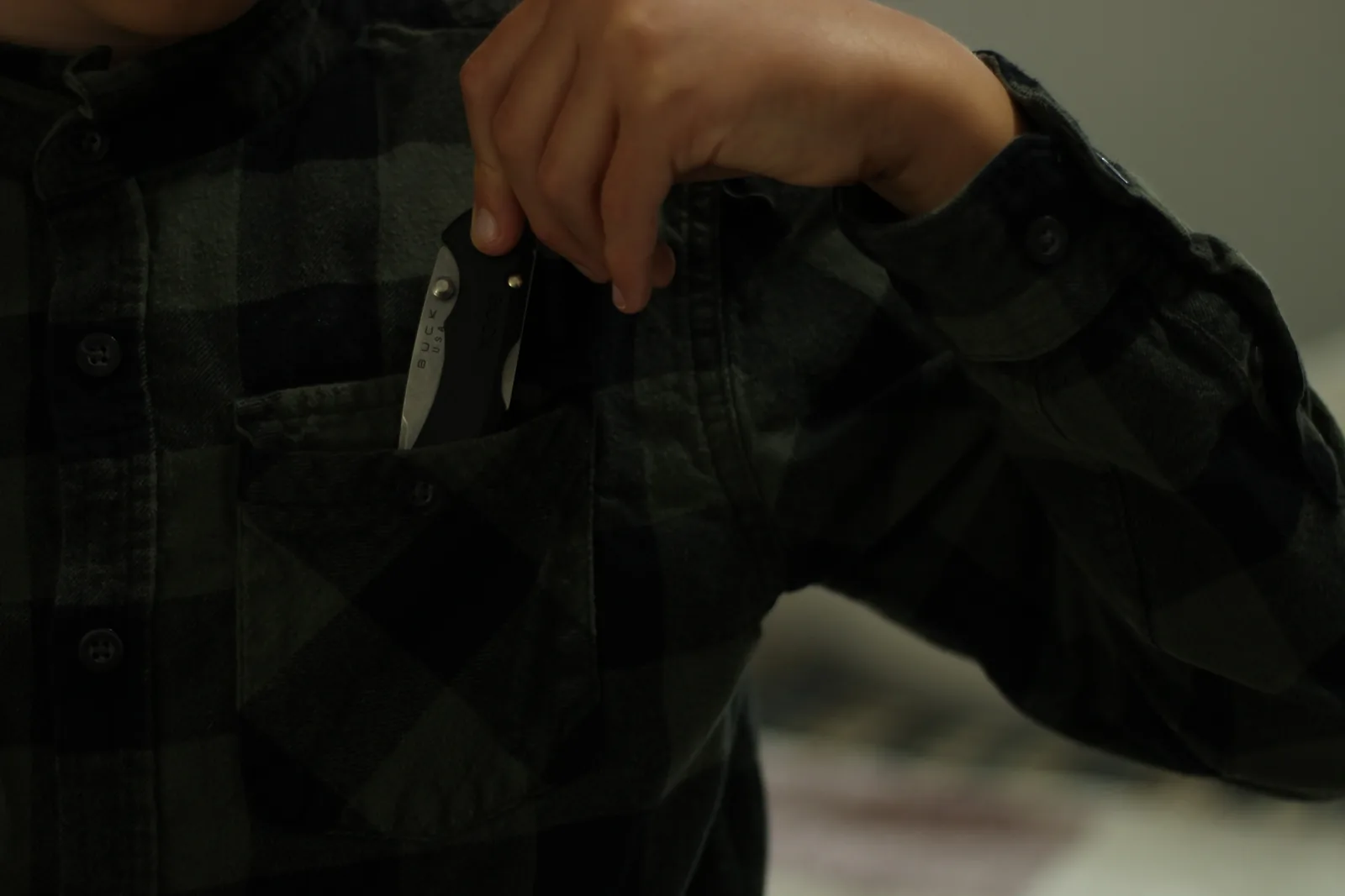The closed knife being lifted out of the chest pocket of a dark green and black flannel shirt