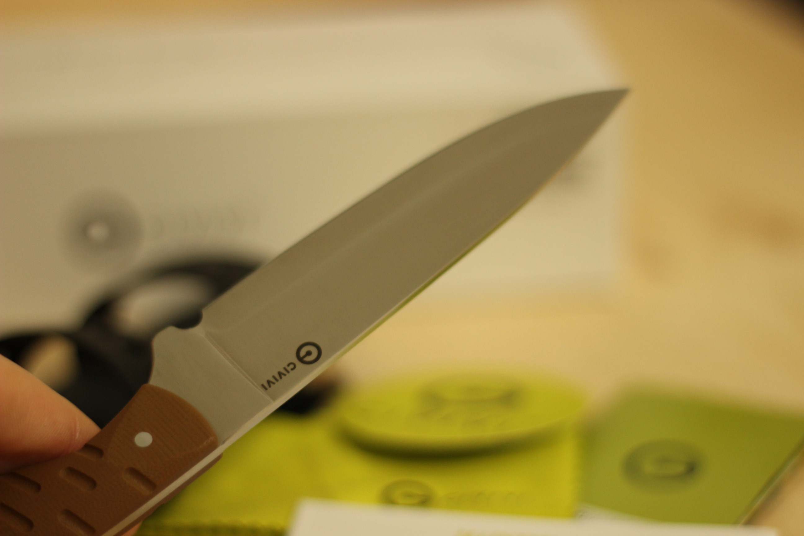 The Civivi MDRN Hunter being deployed from its kydex sheath for the first time, blade exposed to about half-length with the brown G10 handle in hand, the box visible in the background and the green Civivi maintenance literature on the surface