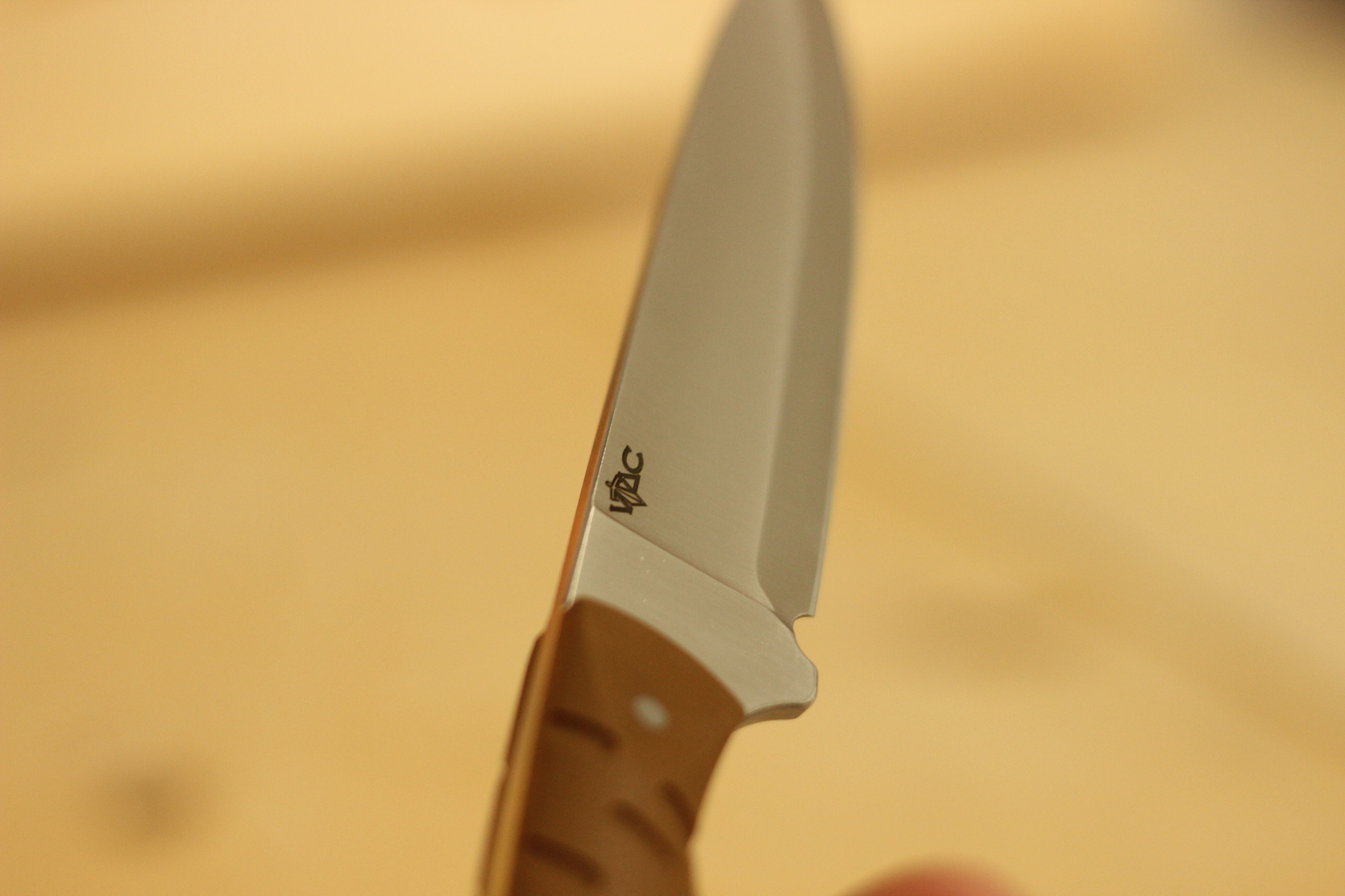The full satin-finished compound-ground drop-point blade of the Civivi MDRN Hunter held vertically against a soft warm out-of-focus background, VTAC logo visible and the brown G10 handle just entering the frame at the bottom