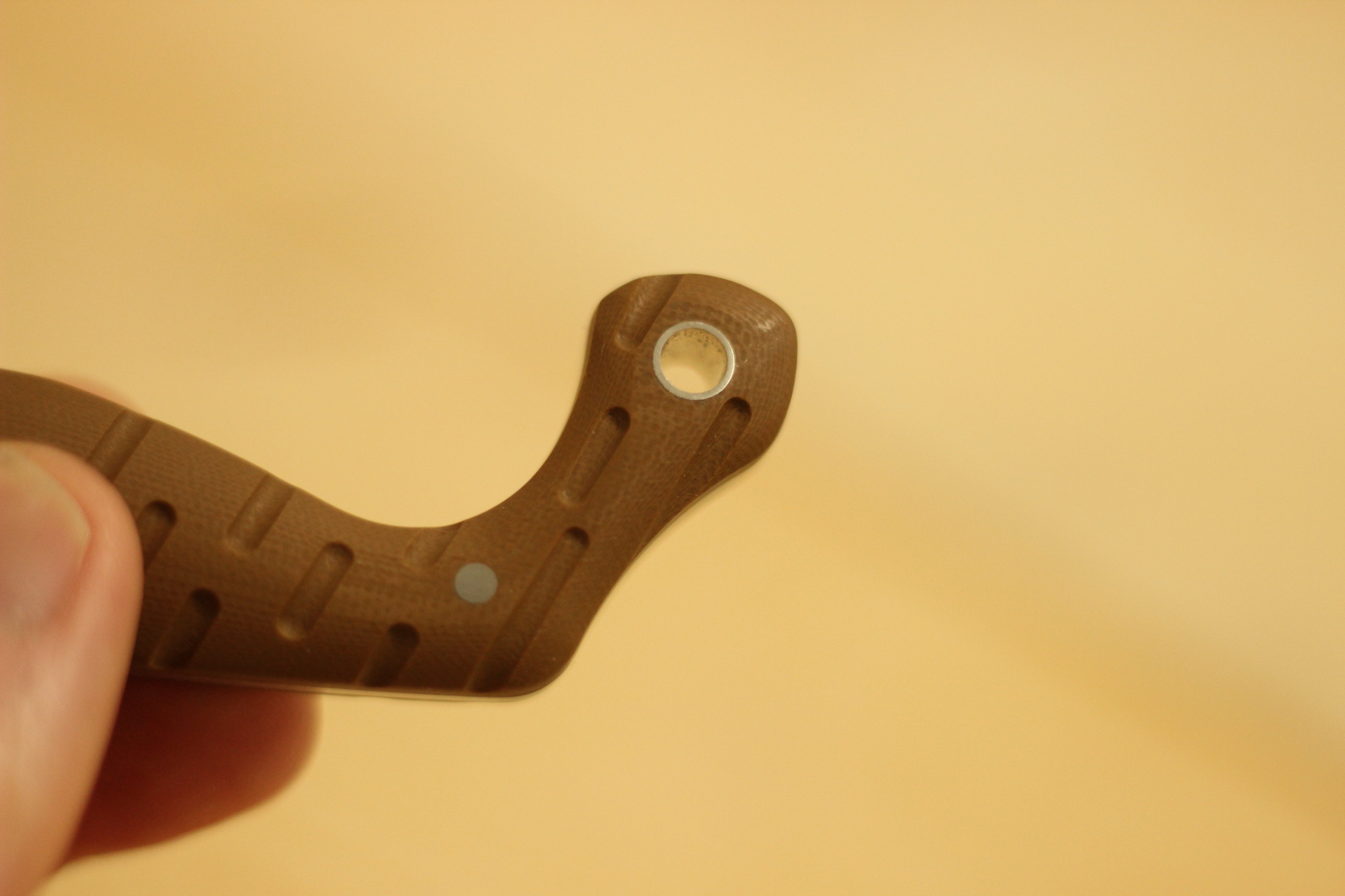 Close-up of the pommel-end of the Civivi MDRN Hunter handle showing the swept hook curve, the steel-lined lanyard hole at the rearmost point, and the deeply machined groove and pin texture on the G10 scale