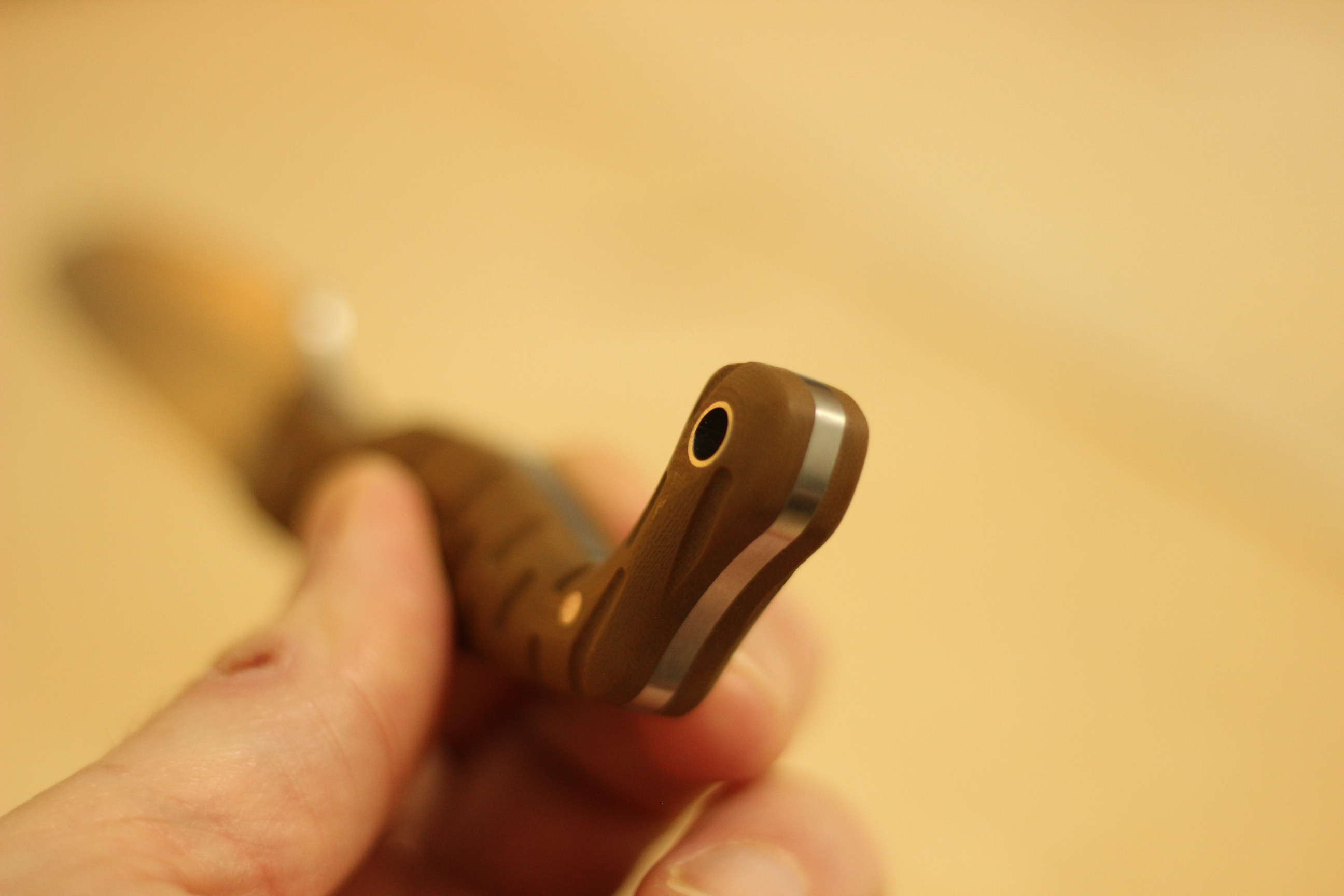 End-on view of the Civivi MDRN Hunter pommel showing the lanyard tube exit hole, the symmetric G10 scales with their groove texture wrapping the tang, and a glimpse of exposed steel at the pommel edge