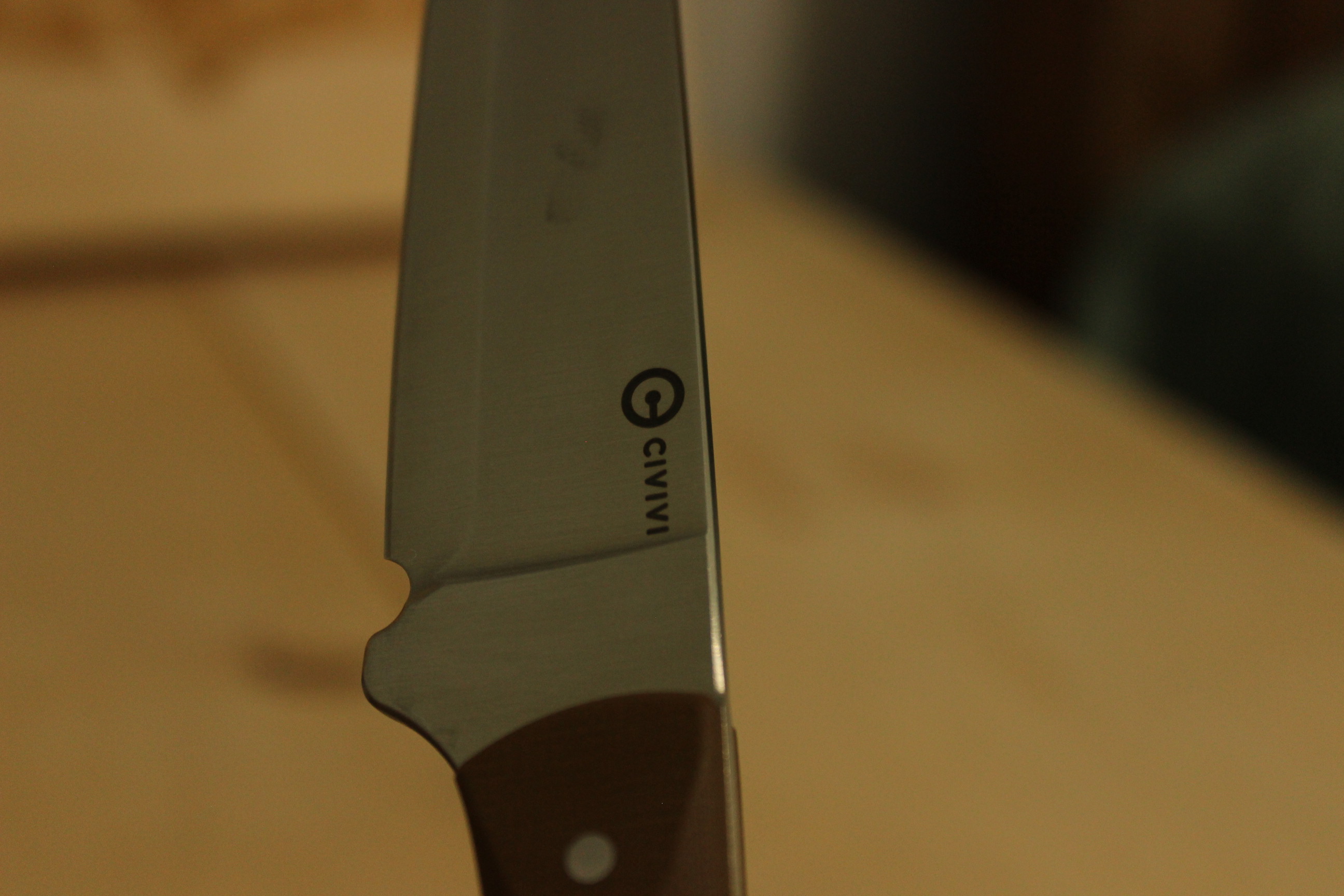 Close-up detail of the finger choil at the heel of the blade where it meets the G10 handle, showing the relieved choil cut and the start of the handle scales
