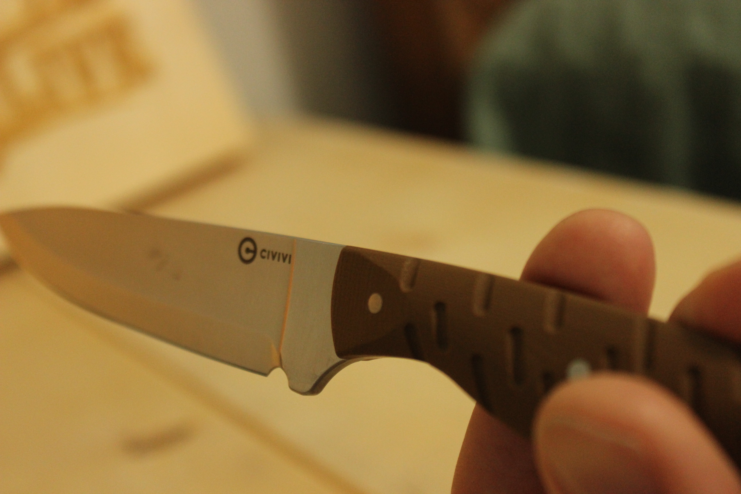 The Civivi MDRN Hunter held in a hammer grip with the brown G10 handle wrapped in the hand, the blade pointing forward toward the camera and the Civivi logo visible on the satin flat