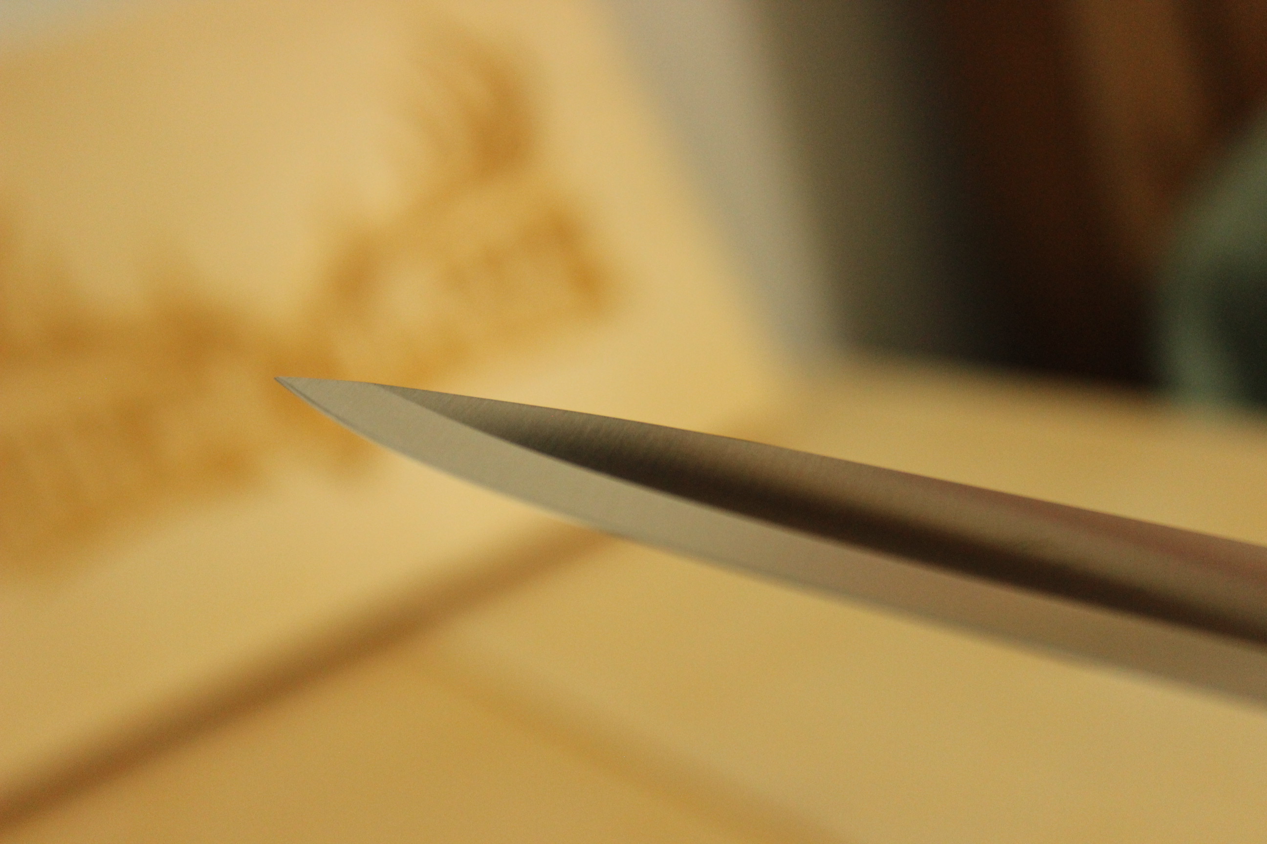 The tip of the Civivi MDRN Hunter blade rendered as a profile silhouette against a warm out-of-focus background — the drop point geometry visible as a single curve dropping to the tip