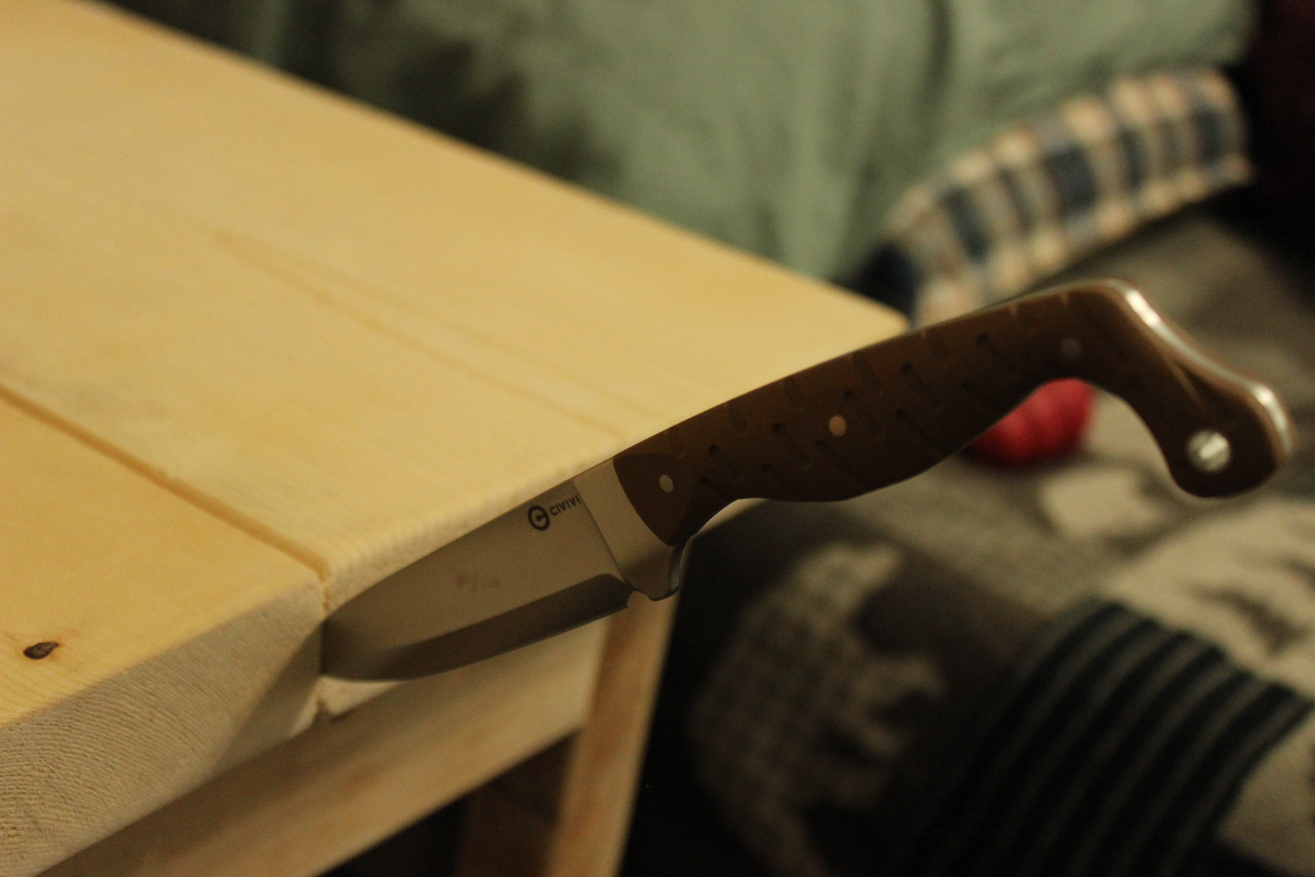 The Civivi MDRN Hunter laid horizontally with its handle overhanging a wood bench edge, the blade flat against the bench top — the proportion of handle to blade visible across the full silhouette