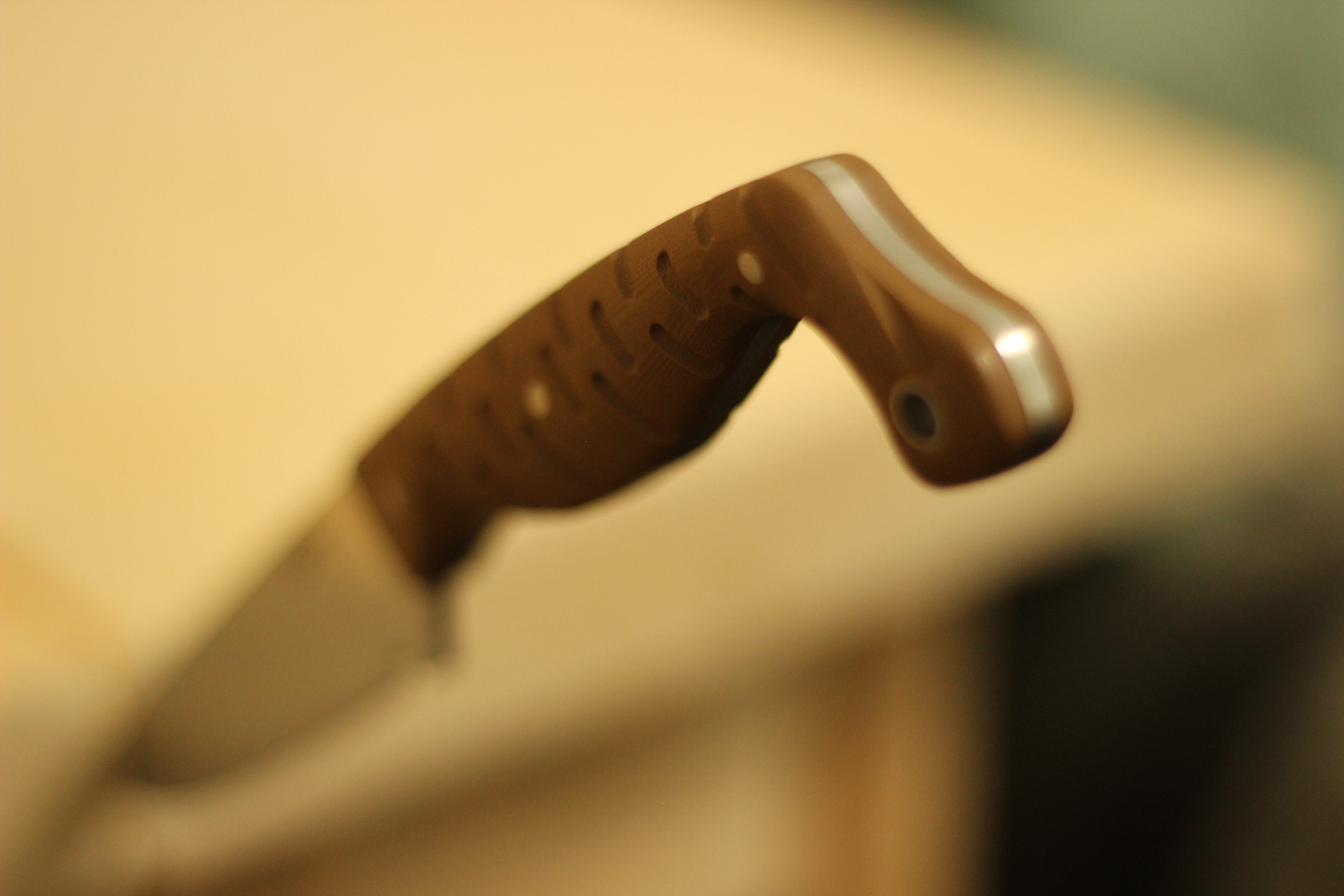 Side profile of the Civivi MDRN Hunter pommel and rear handle section in close-up against a soft cream background, showing the curve of the swept hook and the satin steel pommel edge