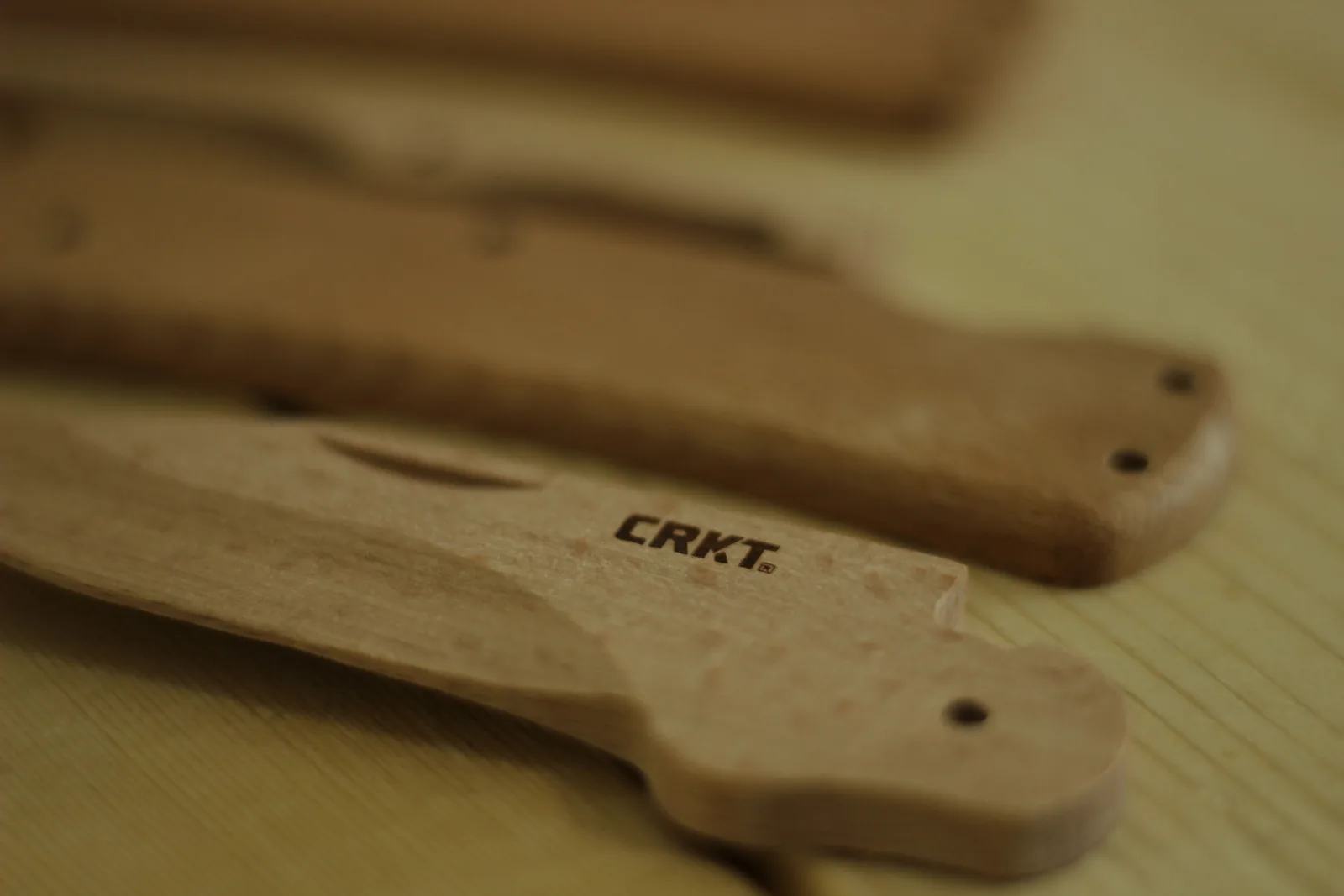 Close-up of the beech blade blank with the CRKT logo burned into the flat, the handle scales lying blurred behind