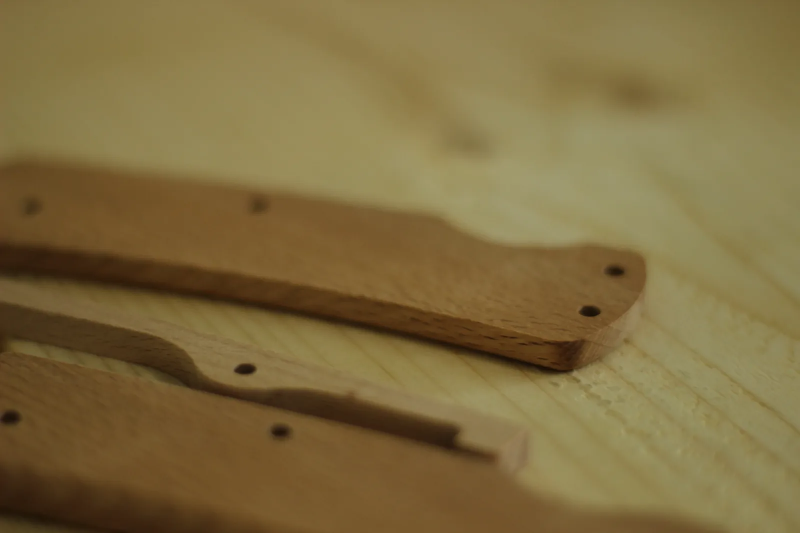 Two beech handle scales on a bench showing the drilled pin holes and the softly rounded edges along their length
