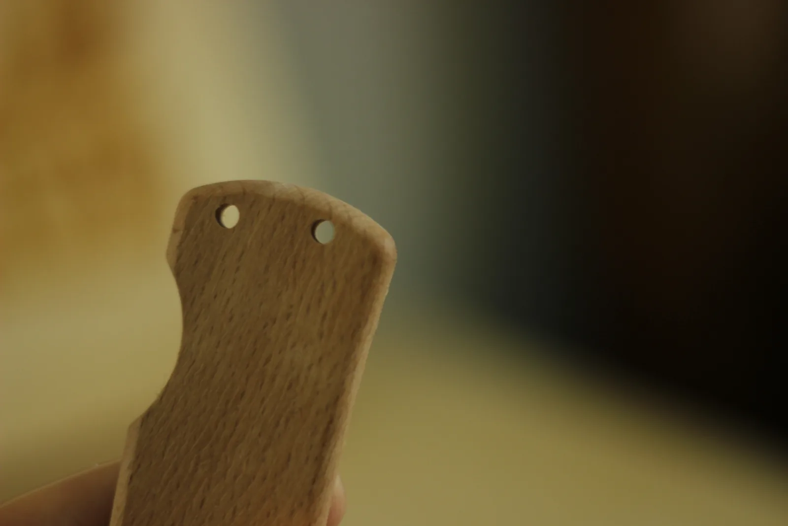 The pivot end of a beech handle scale held up, showing two drilled pin holes and the contoured profile