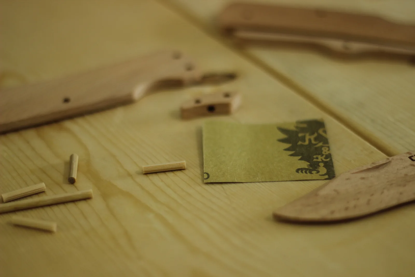 Several short lengths of wooden dowel cut and lying on a bench beside the blade and a scale, with a small green paper square nearby