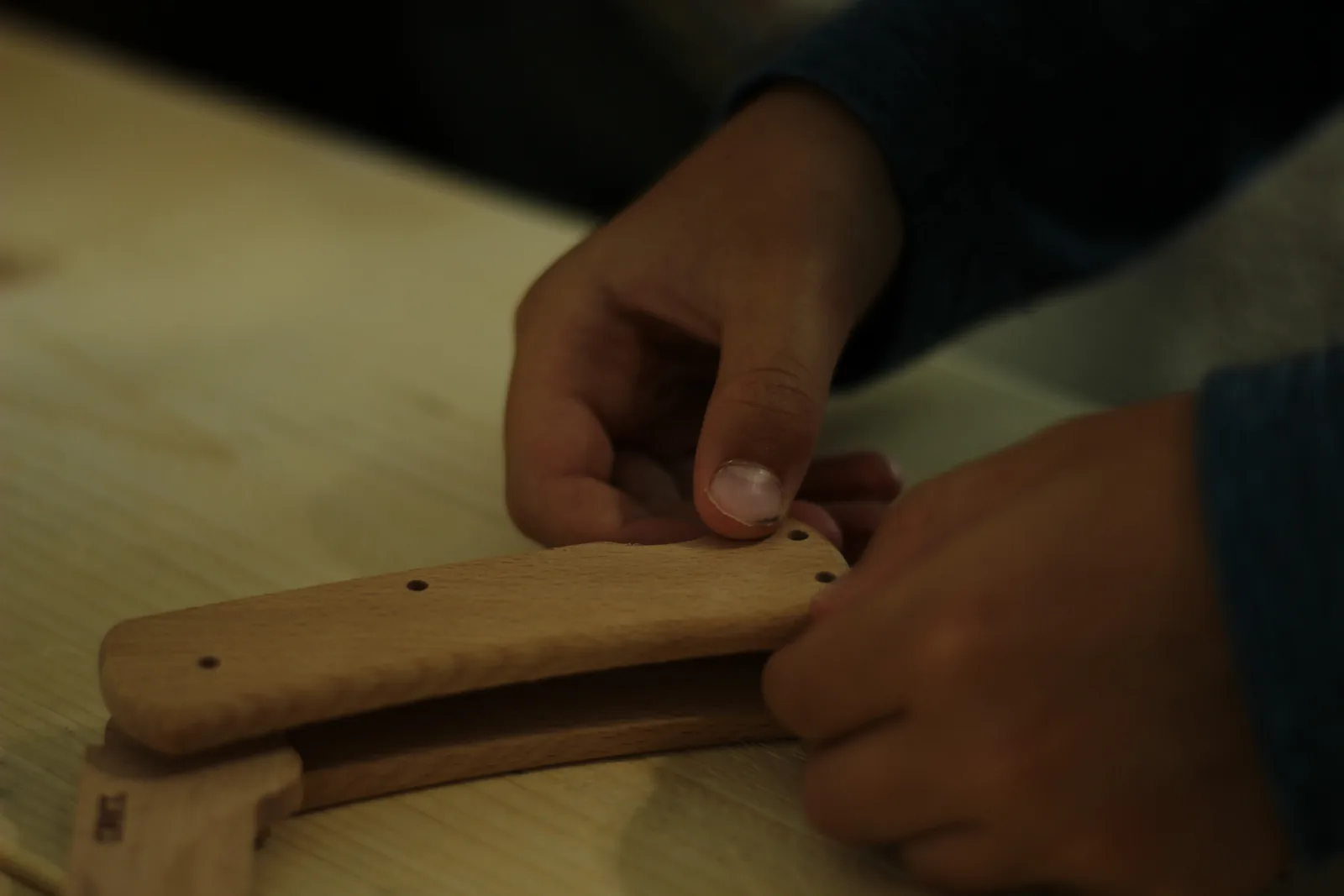Hands pressing the second beech scale down onto the pins of the part-assembled knife