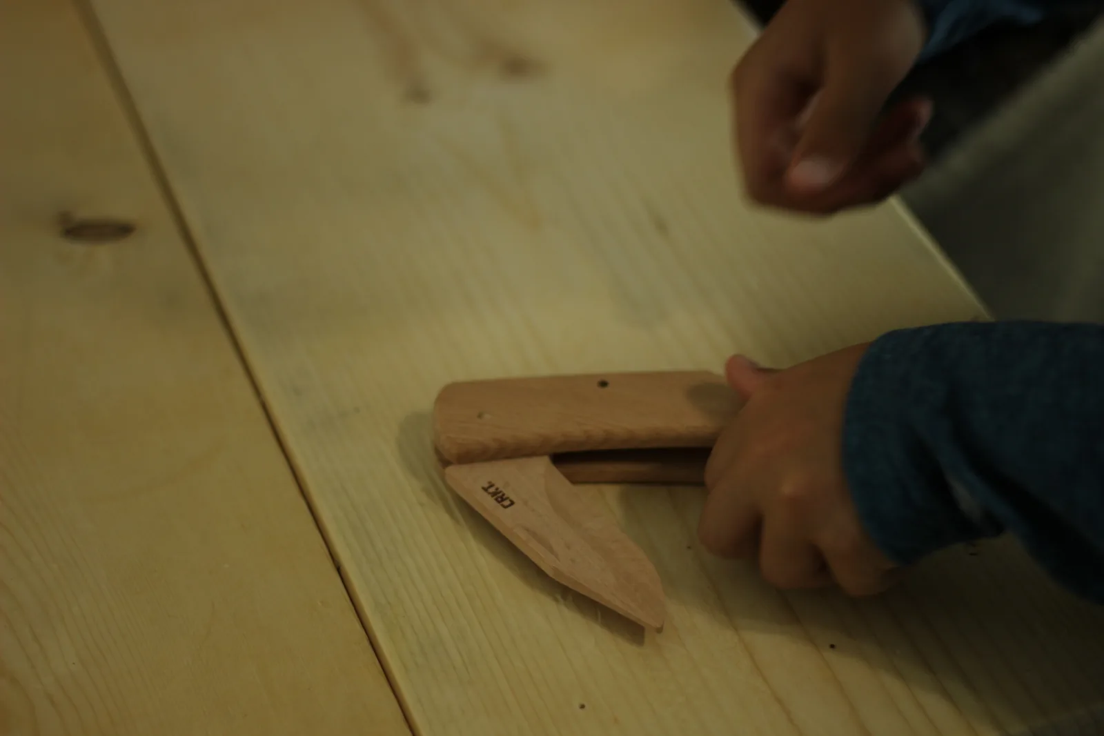 The part-assembled wooden knife on a bench with the blade swung out to the side, a hand steadying the handle