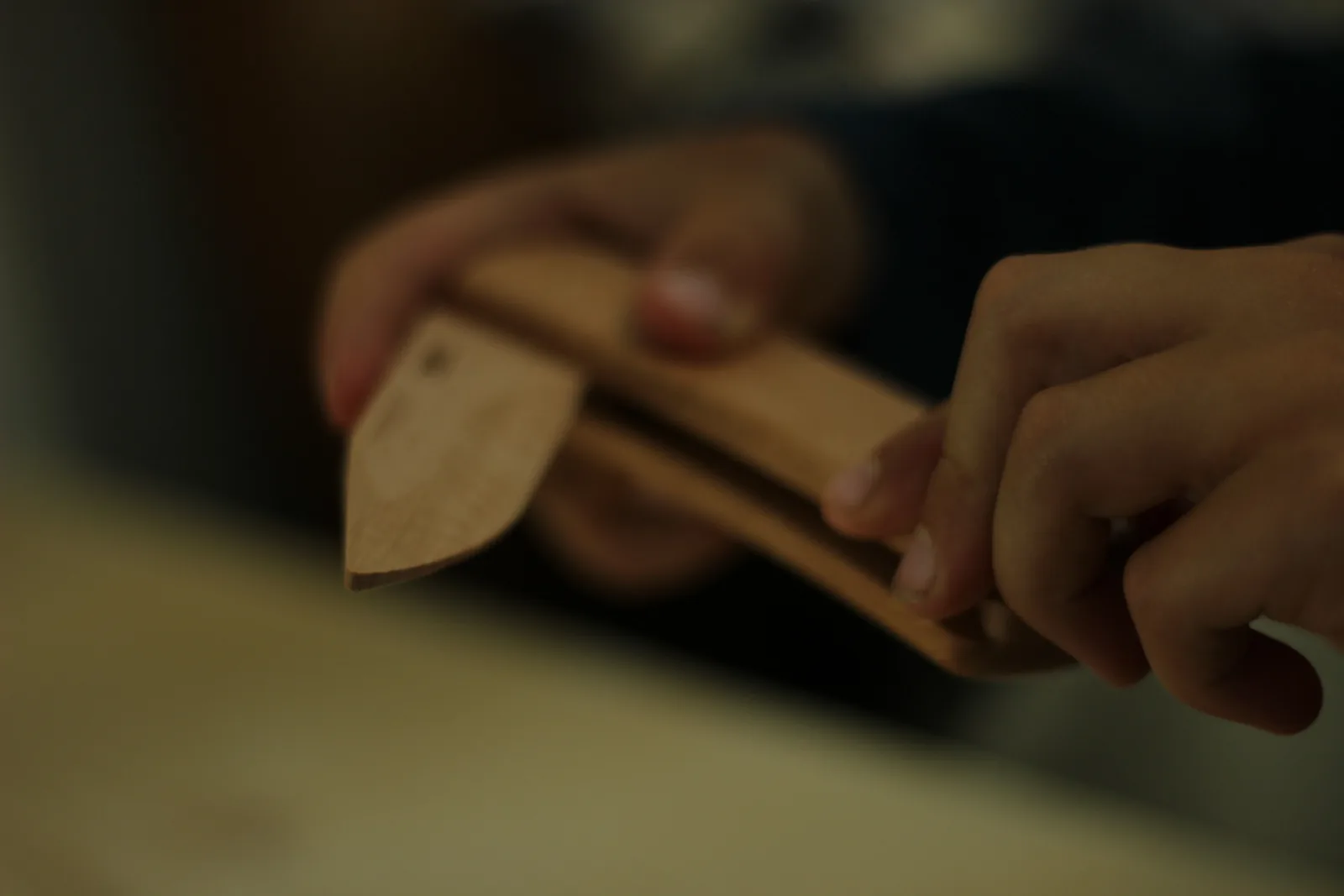 Two hands closing the wooden knife, one pressing the lock bar while the other guides the blade