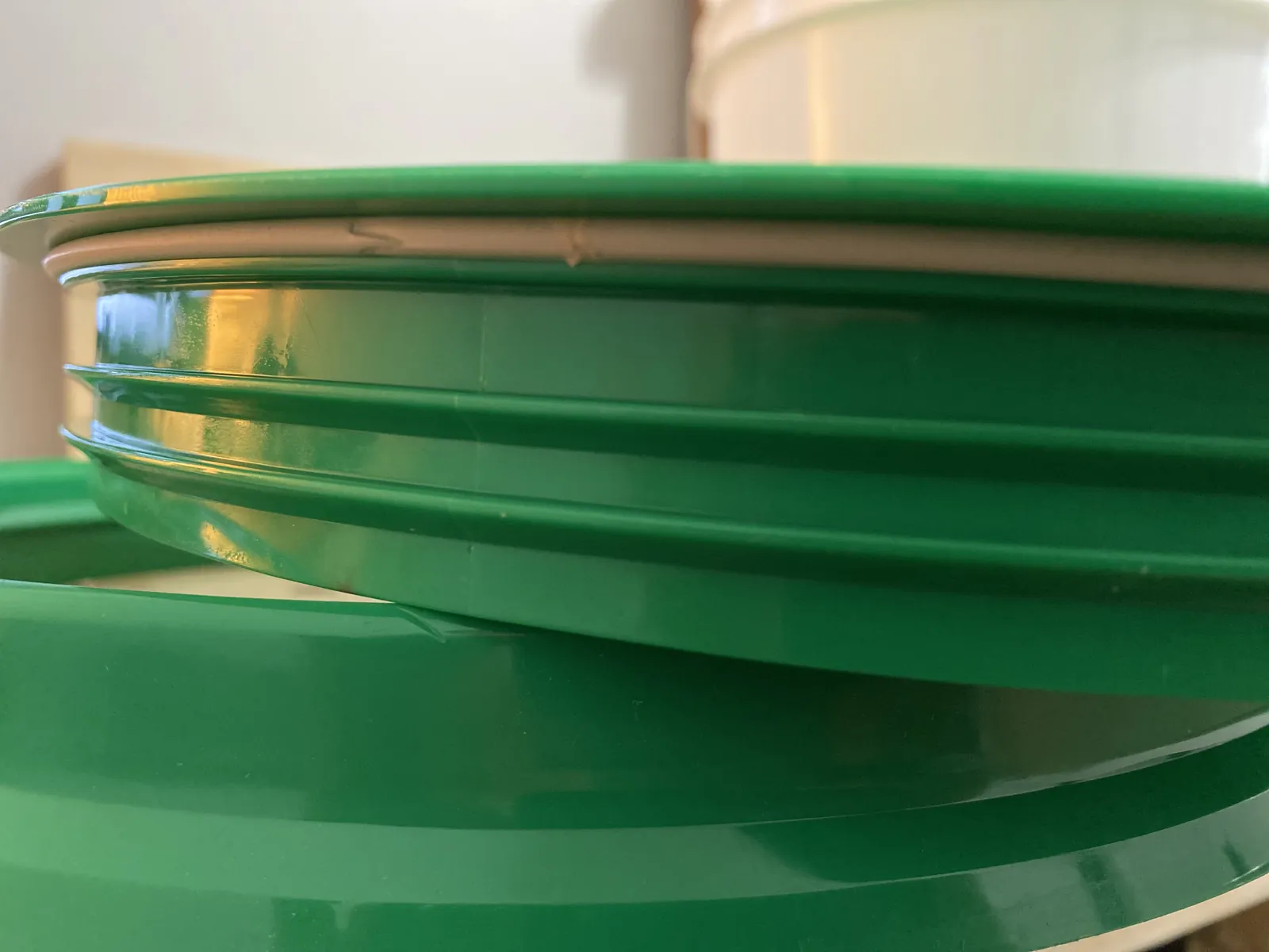 Side view of the GAMMA Seal Lid sitting on top of a white bucket showing the adapter ring snapped onto the rim and the threaded lid above it with a visible gap between the two pieces