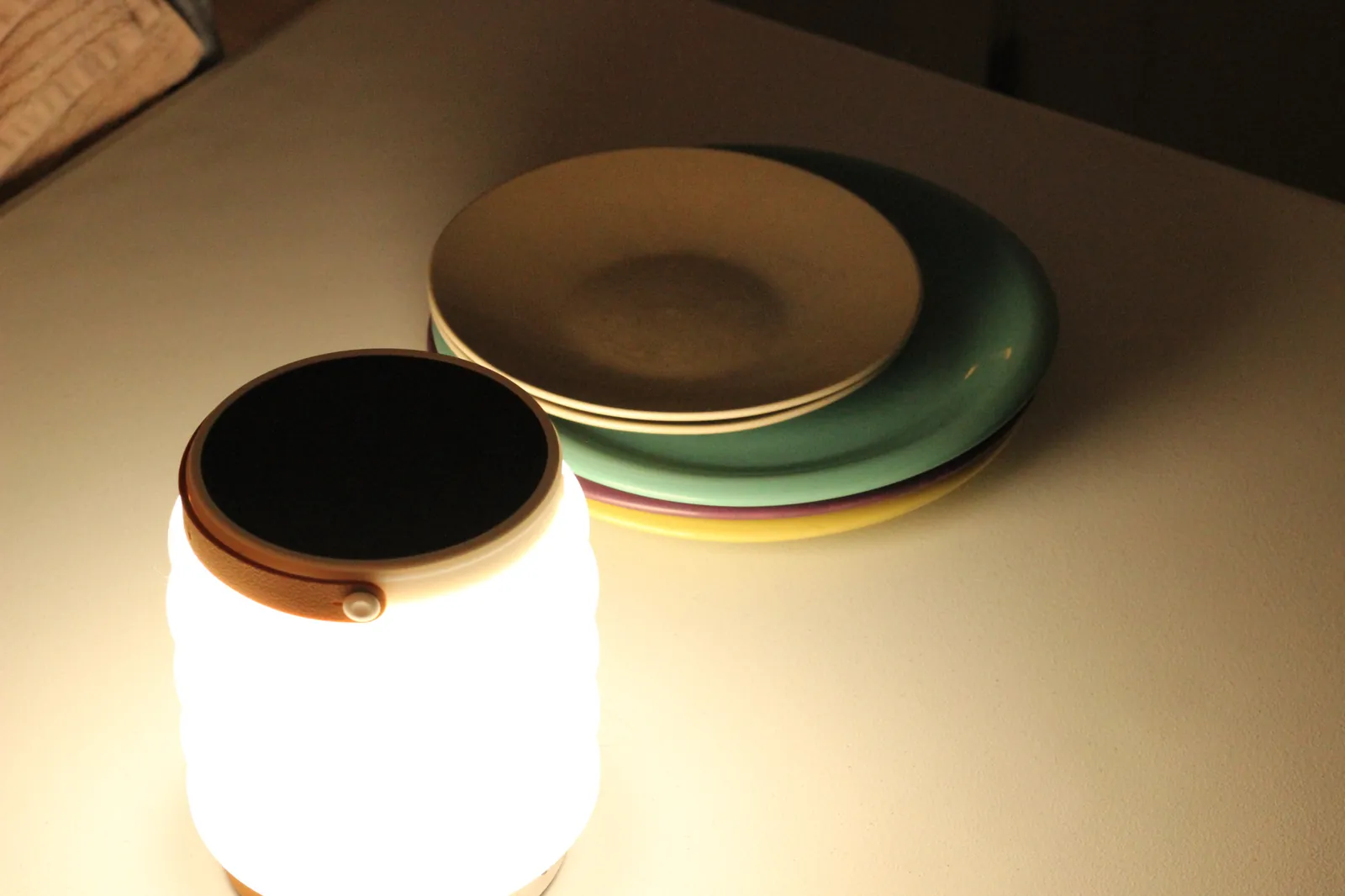 HAVEN 10000 lit on a tabletop beside a stack of colourful ceramic plates showing how the cool-white LED light falls in a normal room