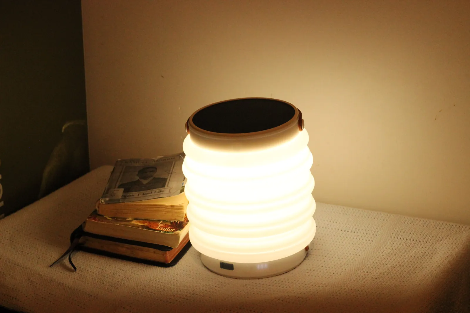 HAVEN 10000 on a bedside table beside a stack of old books, providing reading light against the wall