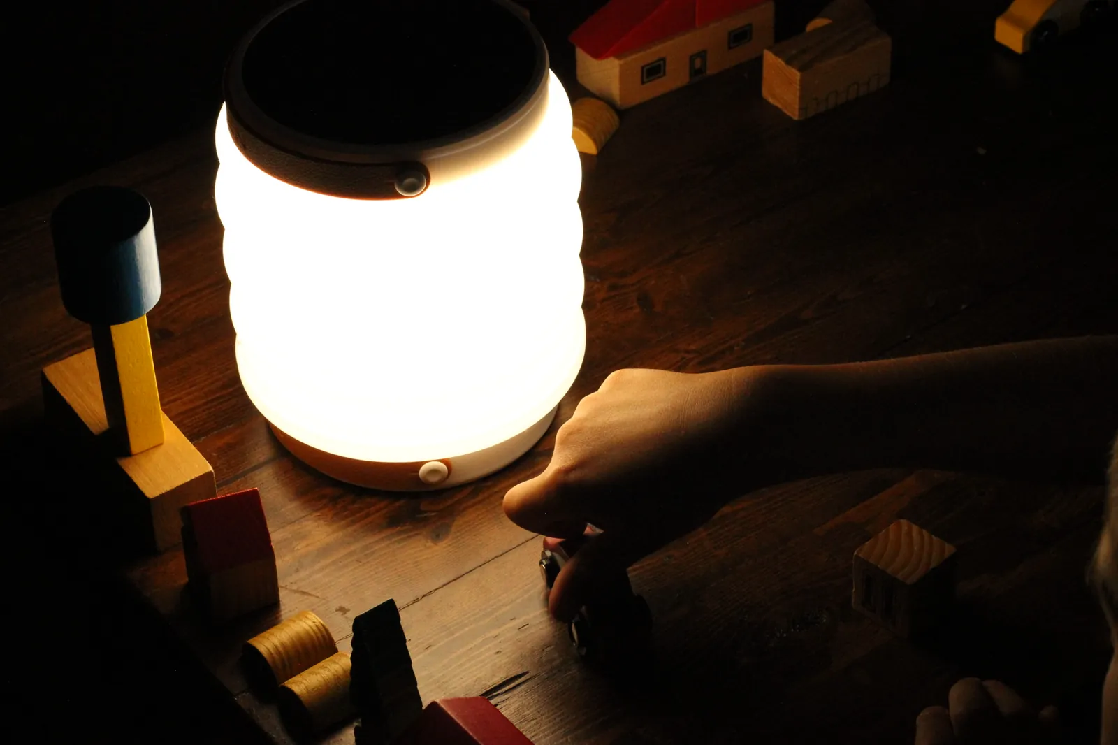 Child building a wooden toy town beside the lit HAVEN 10000 lantern on a wooden table