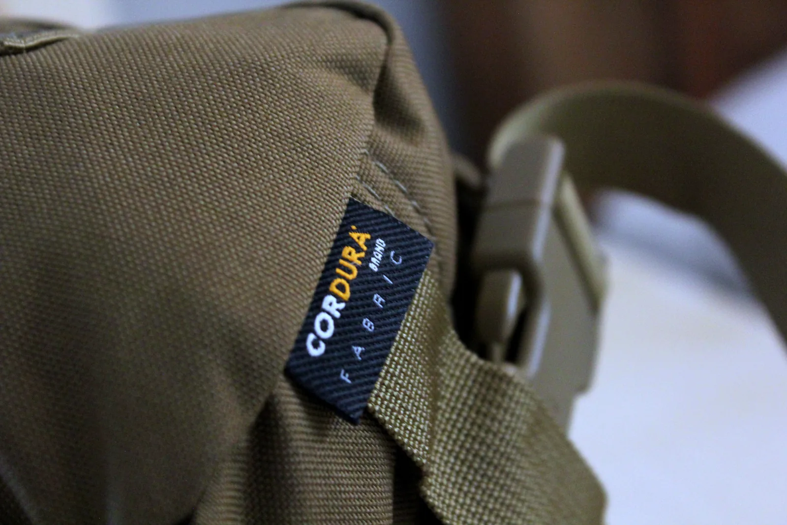 The blue and orange CORDURA FABRIC label stitched into the seam of the olive carry bag