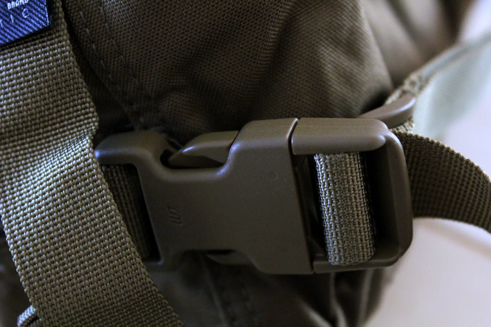Close-up of an olive side-release buckle joining two lengths of webbing on the carry bag strap