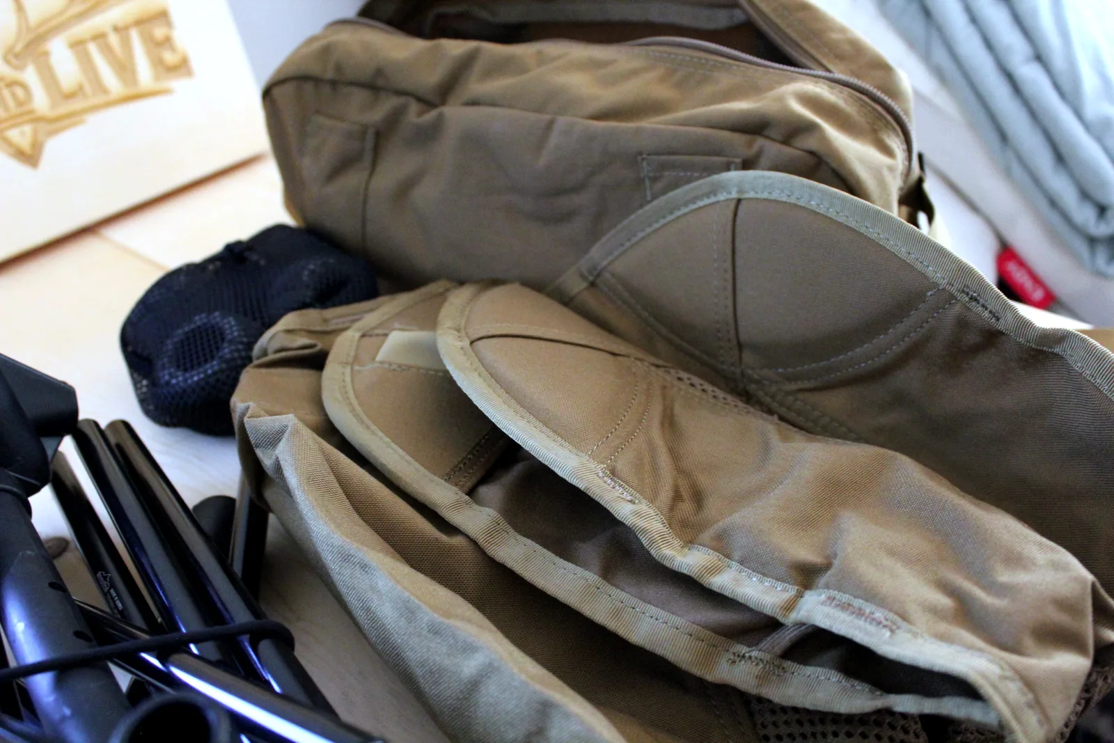 The black shock-corded aluminium pole bundle folded flat next to the coyote Cordura seat