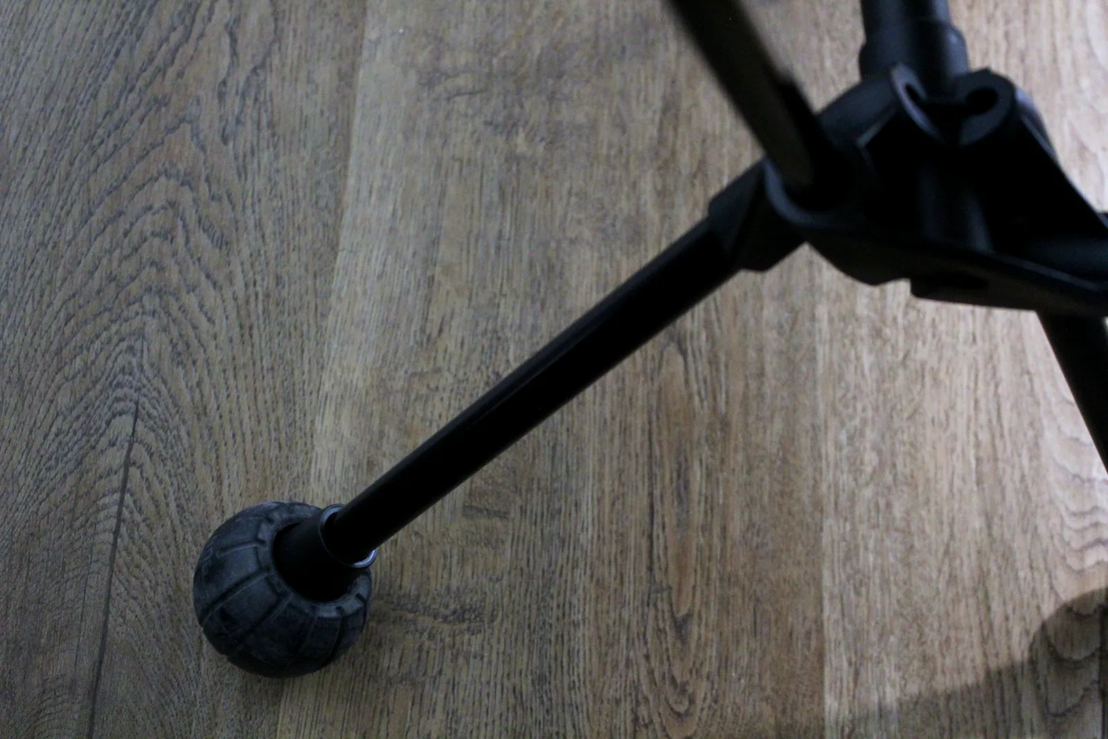 A rubber ball-shaped cap on the end of a black aluminium chair leg resting on a wood floor
