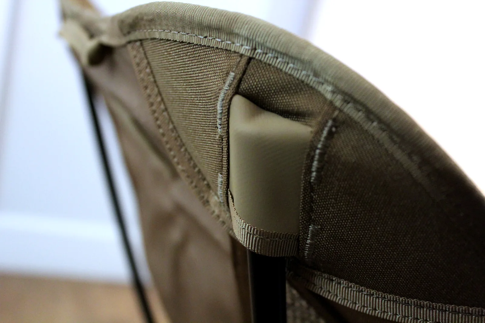 A black aluminium pole end seated into the reinforced corner pocket of the coyote Cordura seat