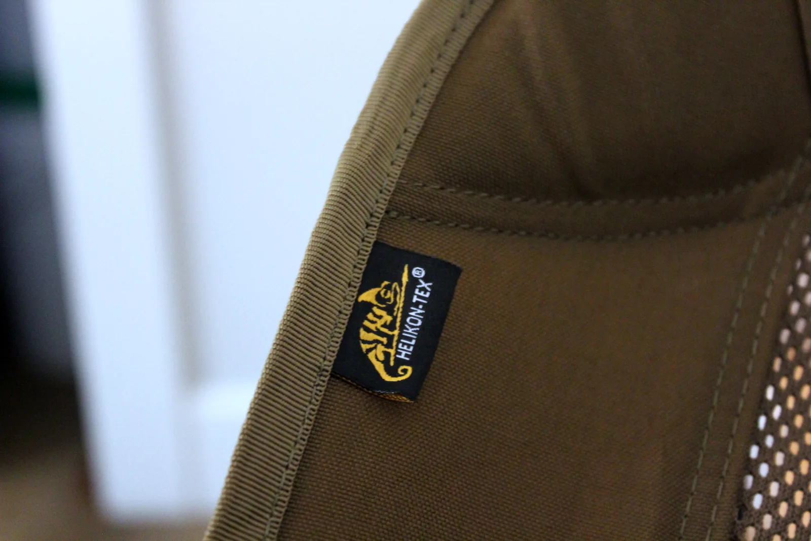 The woven Helikon-Tex chameleon logo label stitched to the outside of the coyote backrest