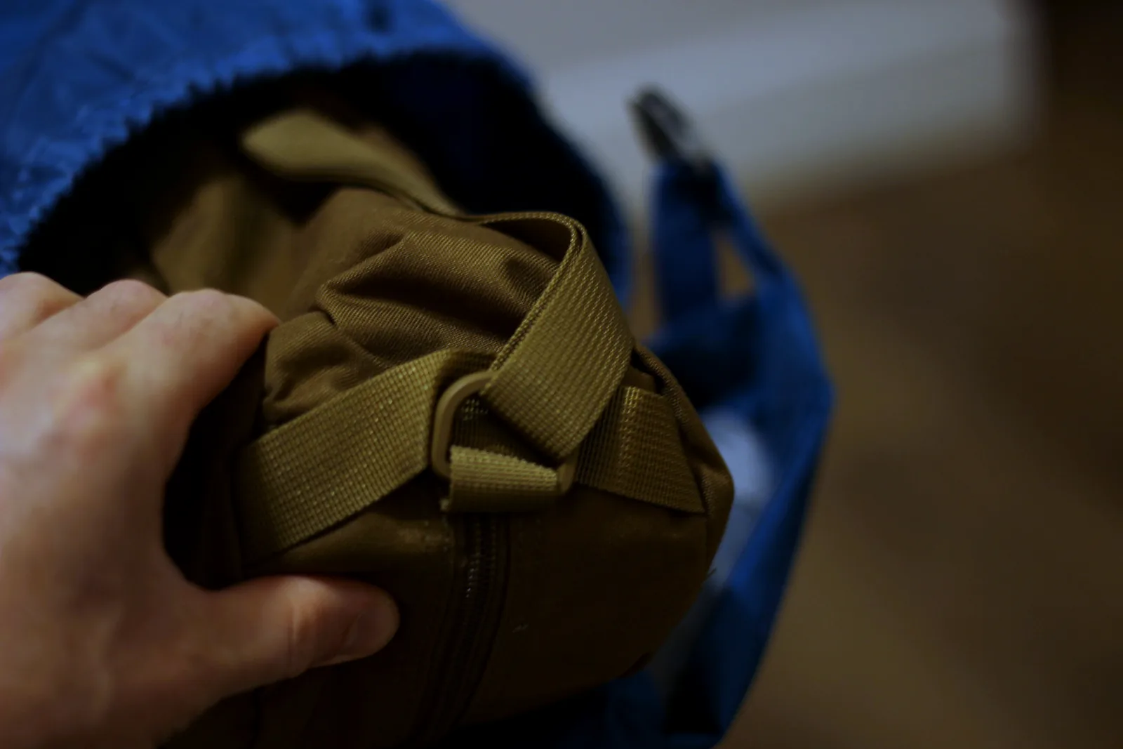 A hand holding the packed olive chair case, roughly the size of a large water bottle