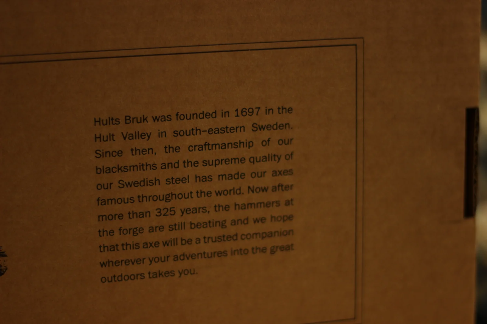 Printed history text on the side of the axe box reading Hults Bruk was founded in 1697 in the Hult Valley in south-eastern Sweden, with text continuing about Swedish steel and 325 years of forging